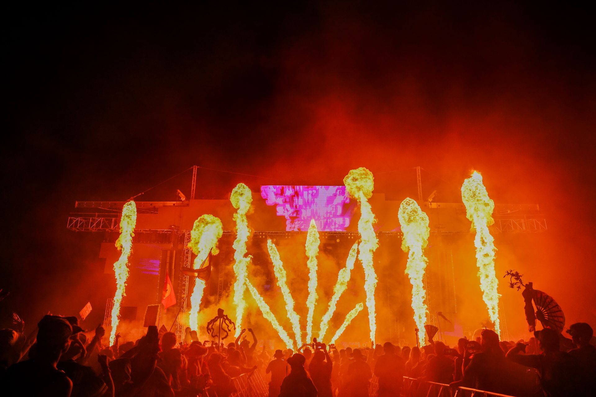 A crowd of people are standing in front of a stage with fire coming out of it.