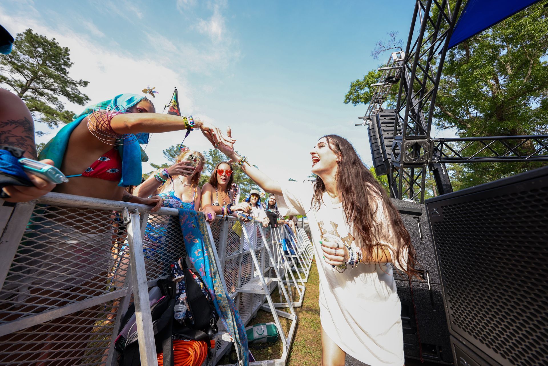A woman in a white dress is shaking hands with a crowd of people at a music festival.
