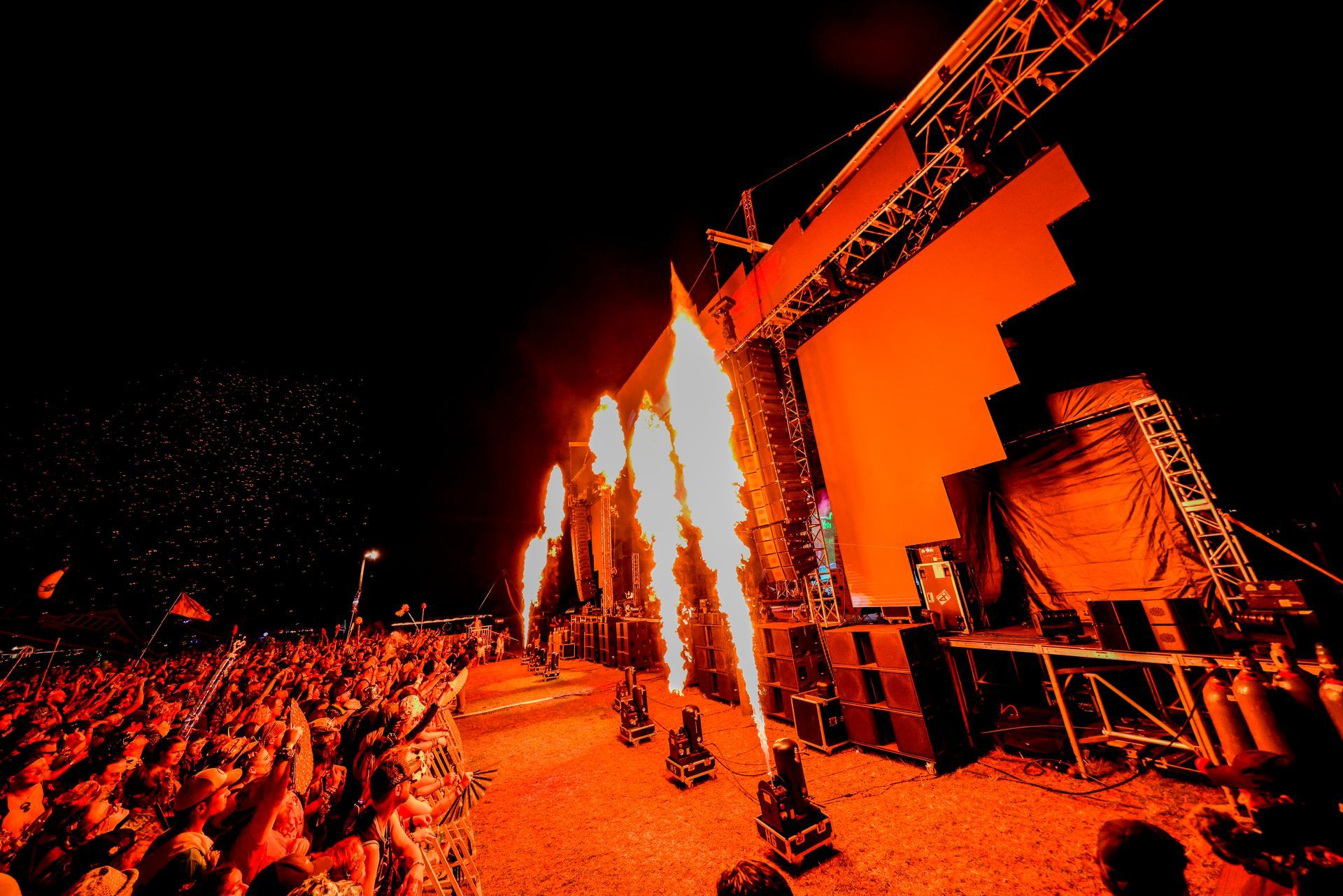 A crowd of people watching a concert with flames coming out of the stage.
