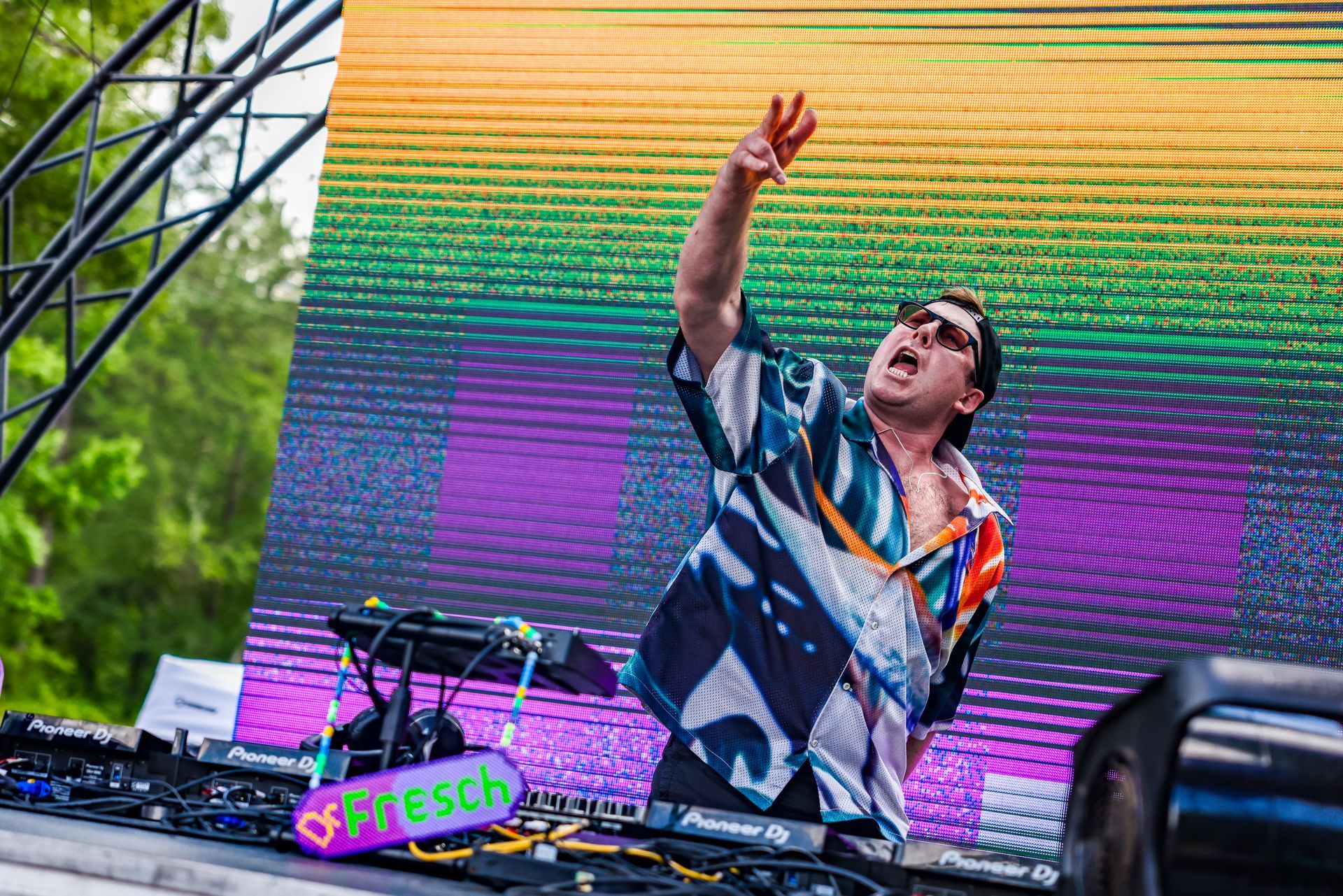 A man is standing in front of a large screen playing a dj set.