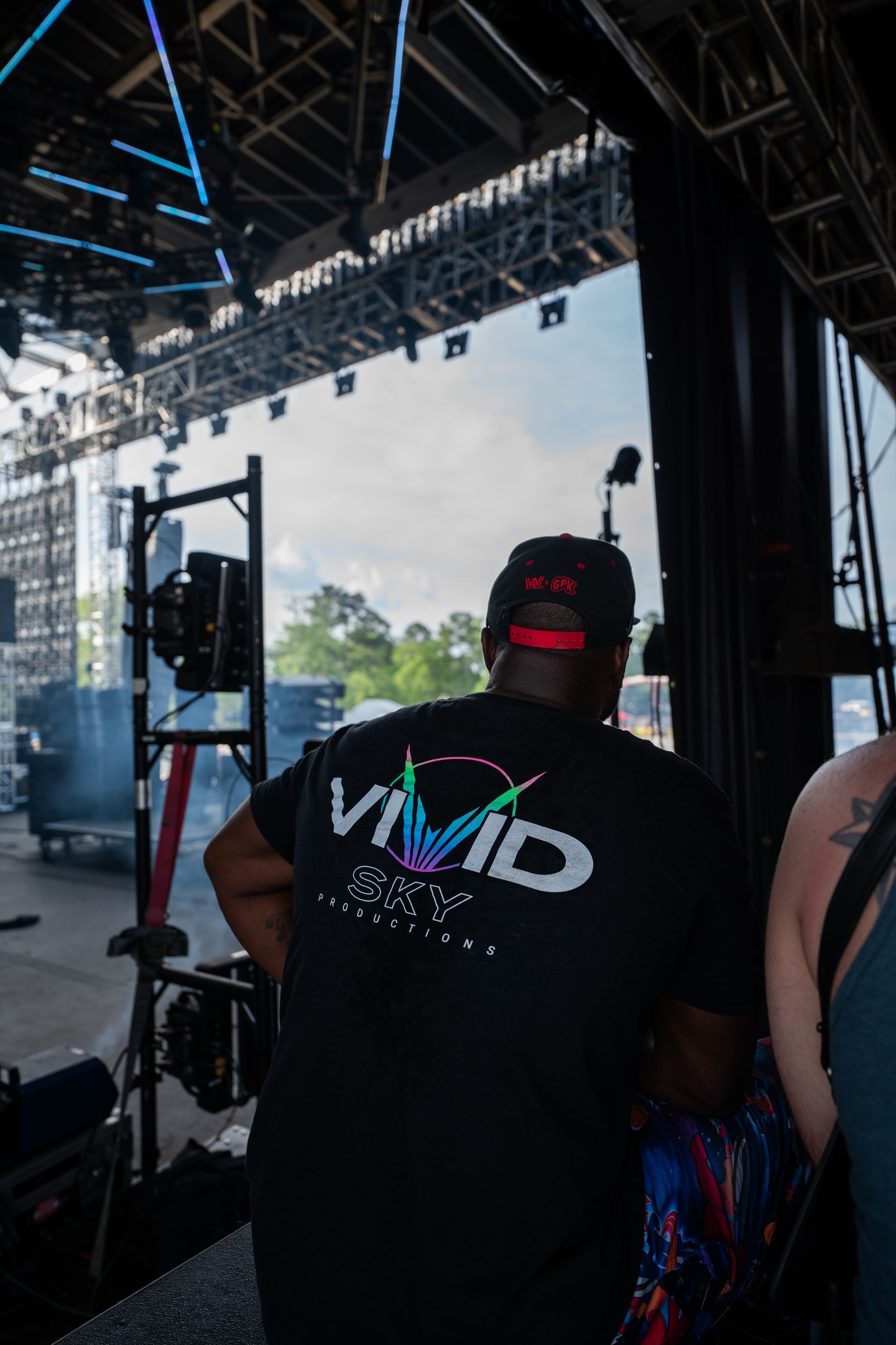 A man wearing a vivid shirt is standing in front of a stage.