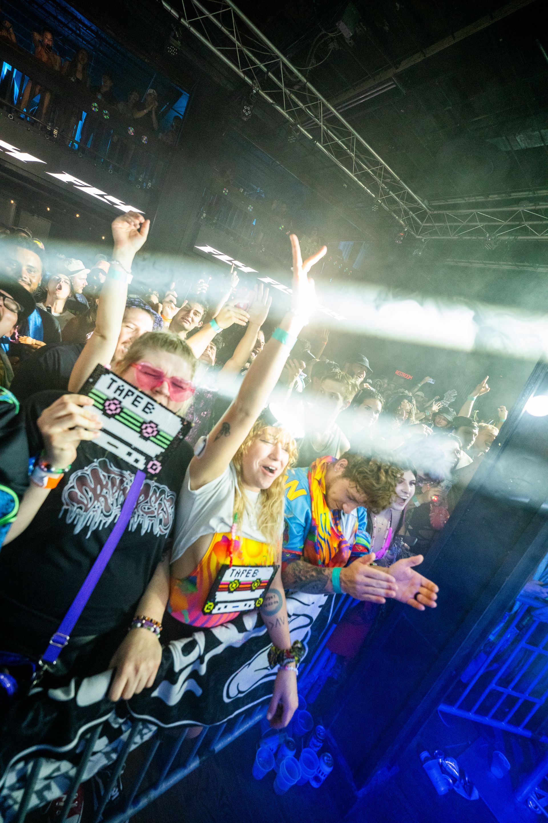 A crowd of people are standing in a dark room with their arms in the air.