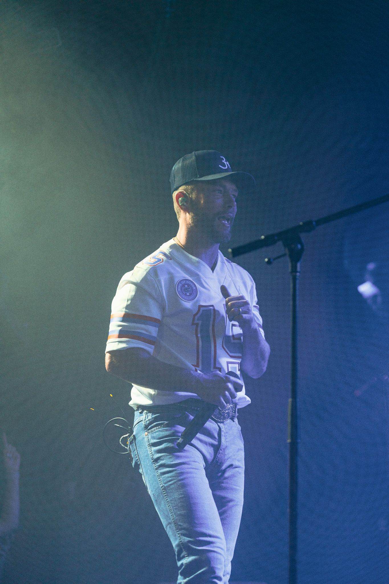 A man in a baseball cap is singing into a microphone on a stage.