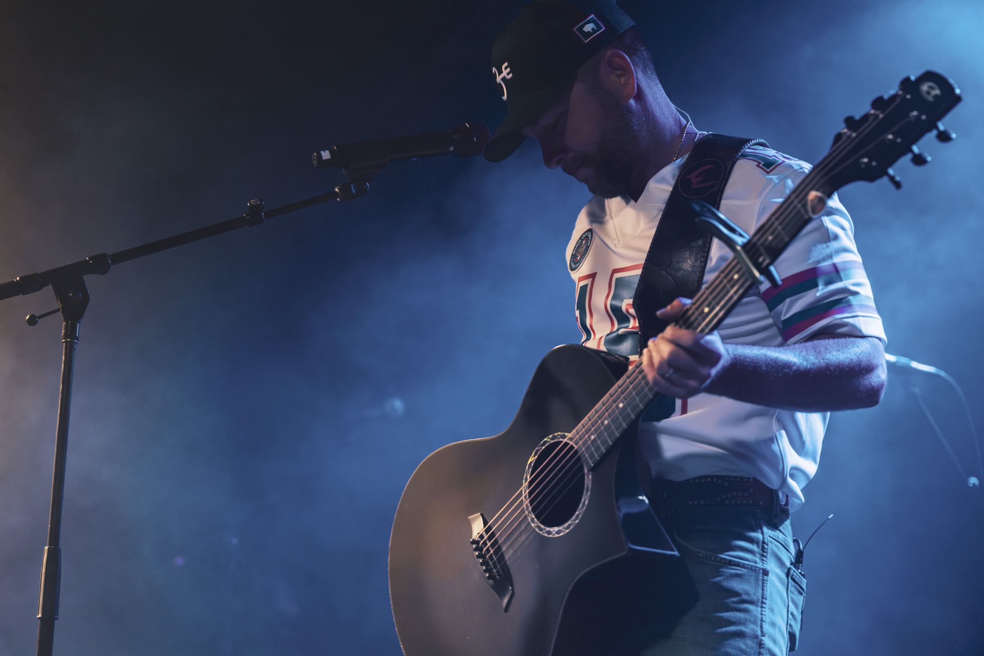 A man is playing an acoustic guitar on a stage in front of a microphone.