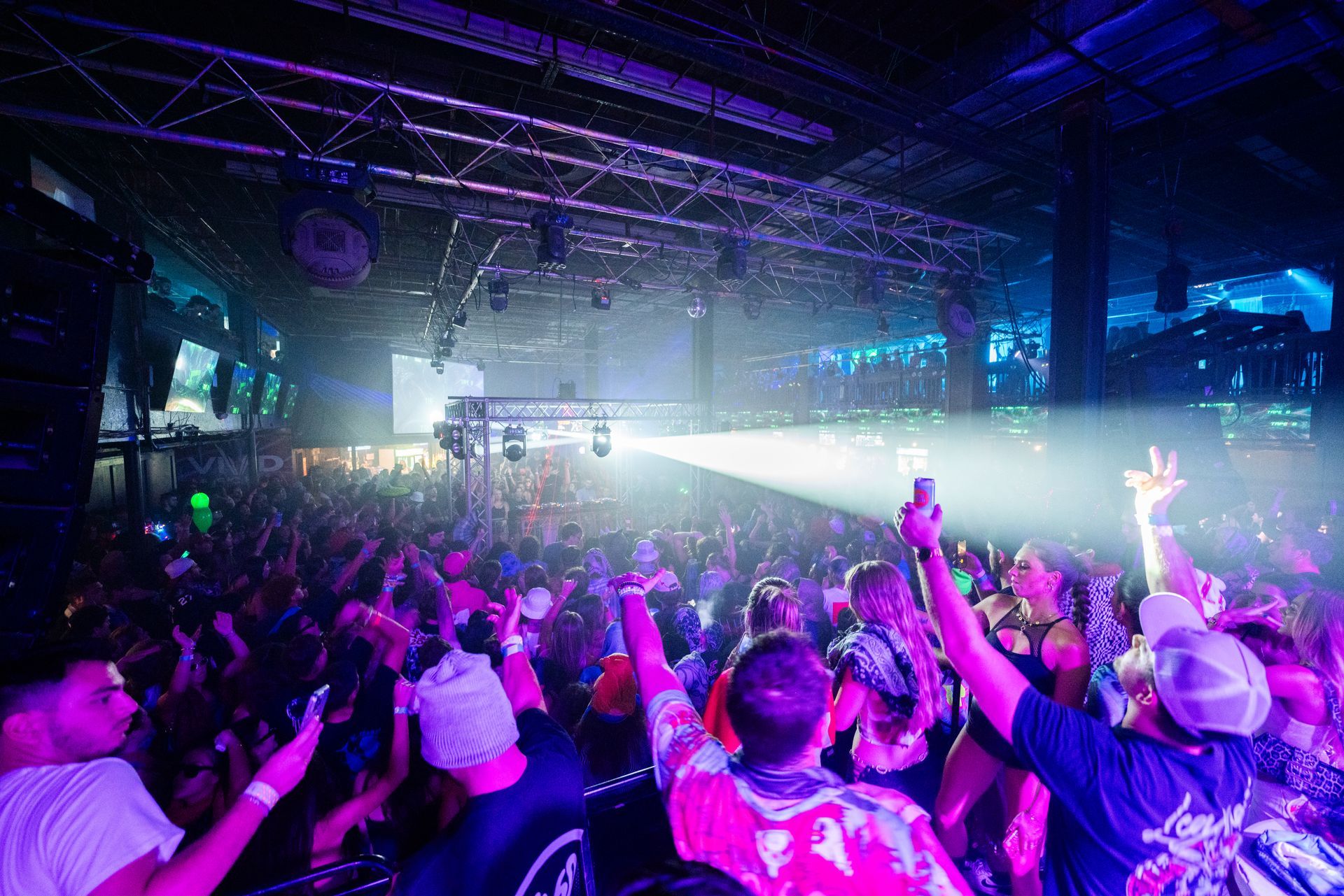 A crowd of people are dancing in a club with their hands in the air.