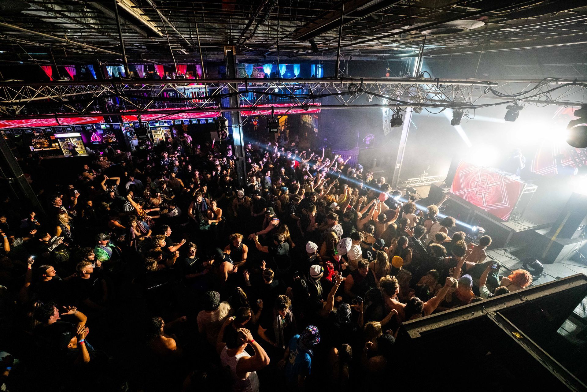A large crowd of people are standing in a dark room at a concert.