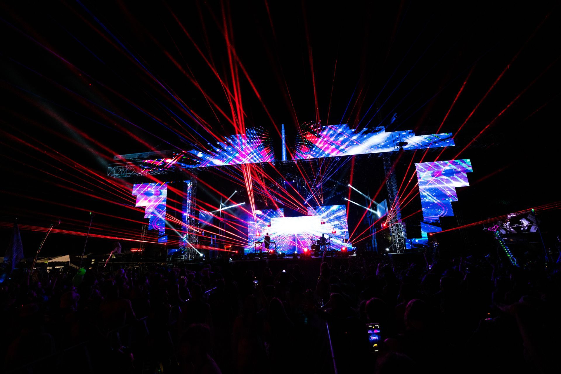 A crowd of people are watching a concert with a lot of lights on the stage.