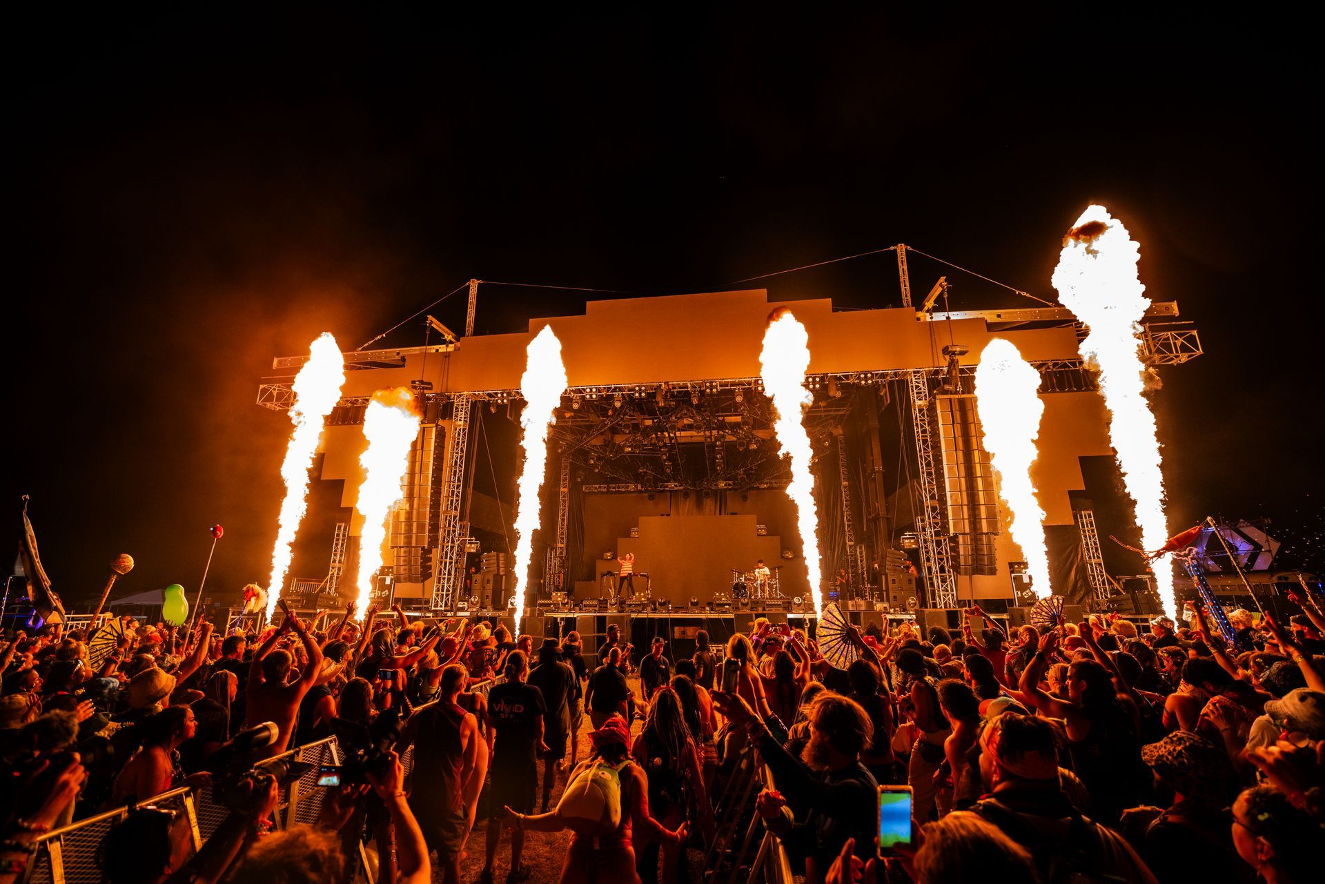 A crowd of people at a concert with flames coming out of the stage