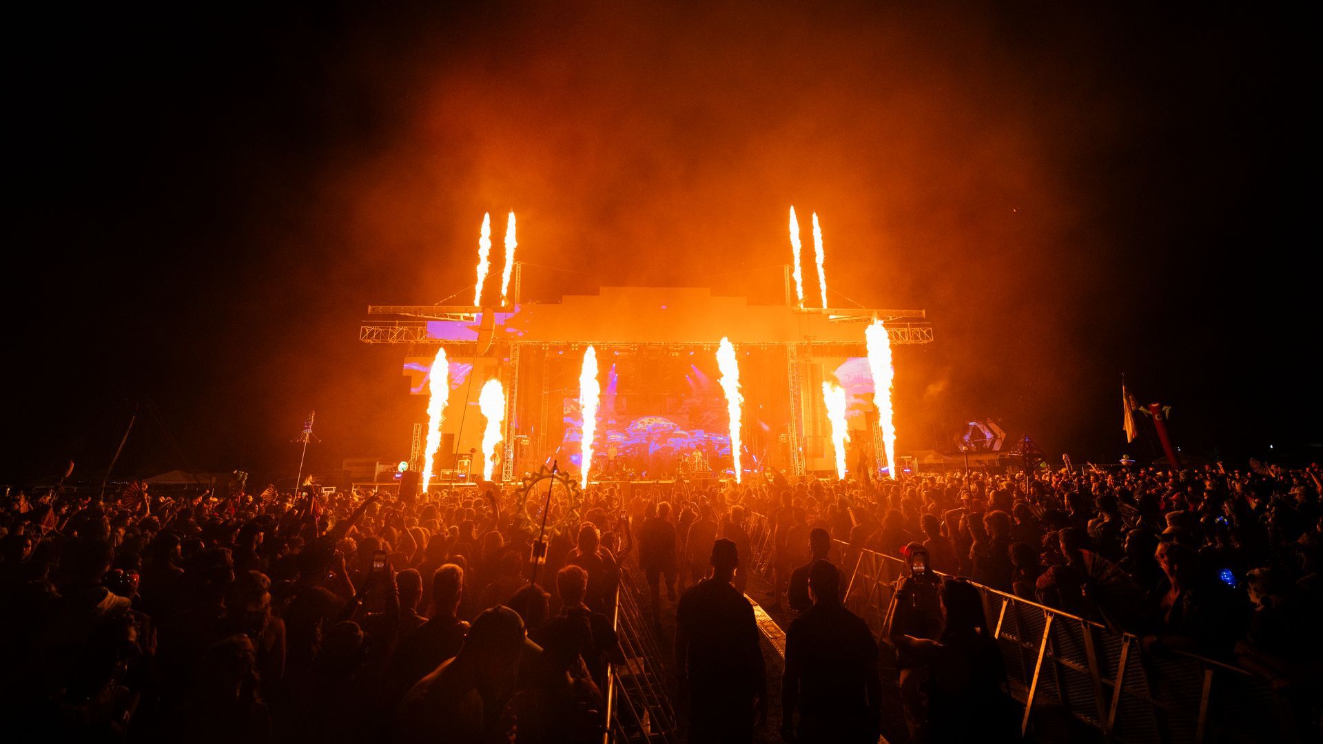 A crowd of people are standing in front of a stage with fireworks coming out of it.