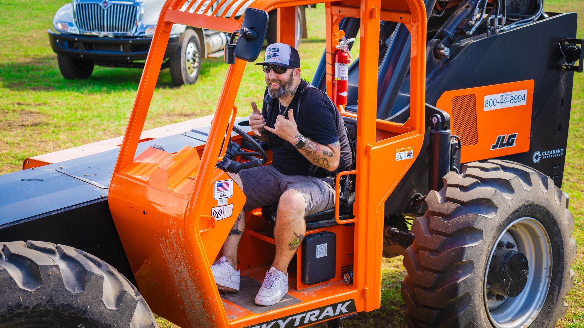 A man is sitting in an orange tractor giving a thumbs up.