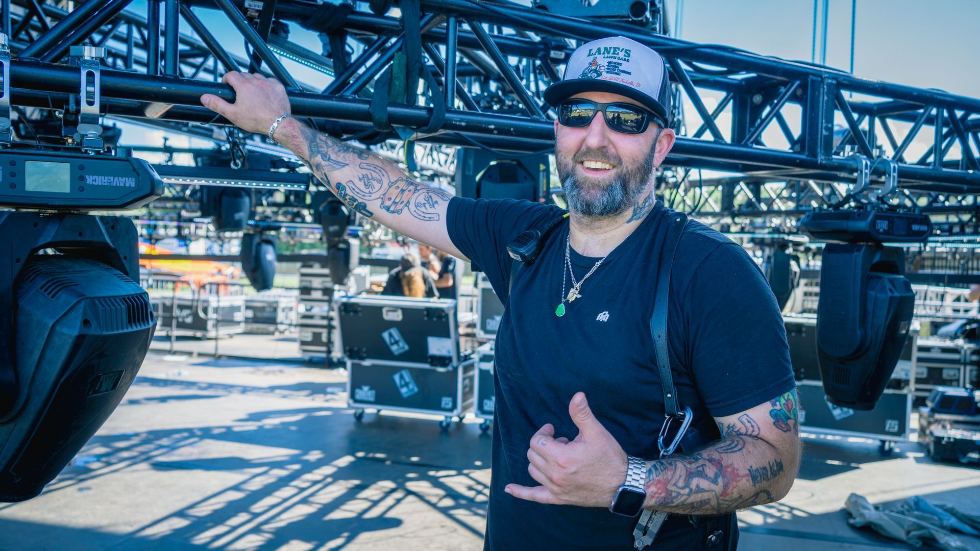 A man with tattoos is standing in front of a stage giving a thumbs up.