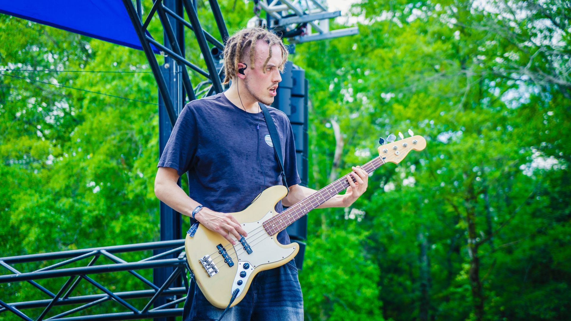 A man is playing a guitar on a stage in front of trees.