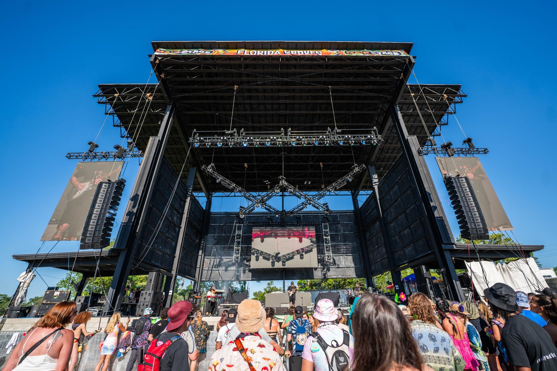 A crowd of people are standing in front of a large stage at a music festival.