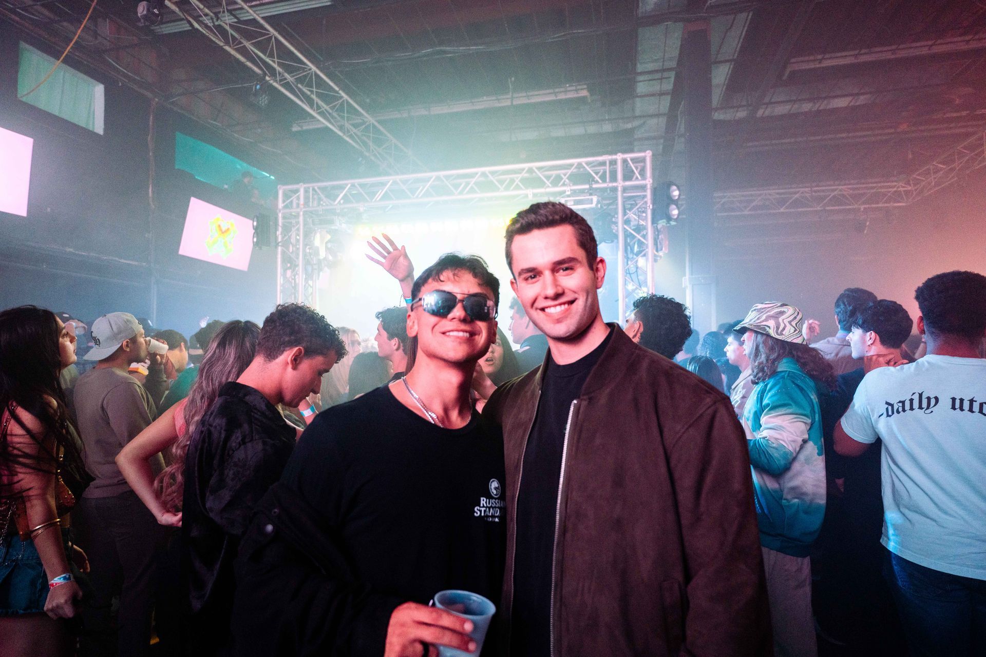 Two men are posing for a picture in a crowded room at a party.