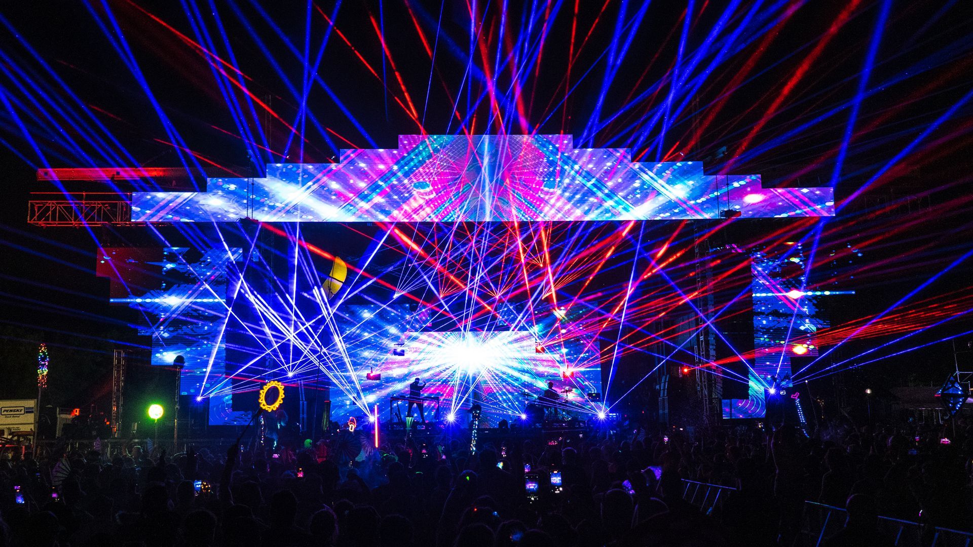 A crowd of people are watching a concert with a lot of lights on the stage.