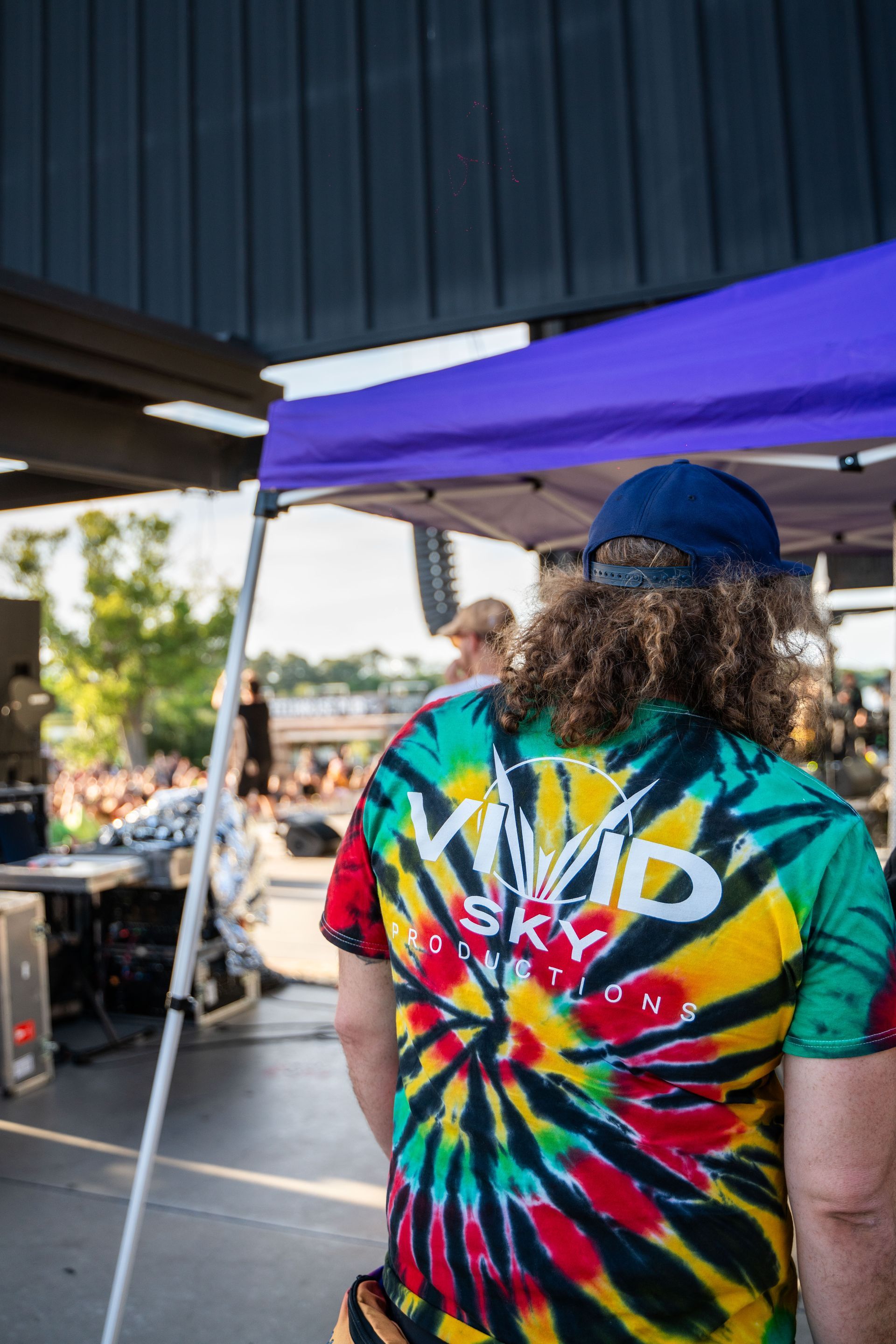 A man wearing a tie dye shirt is standing under a tent.