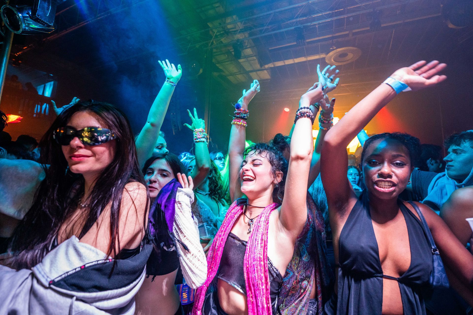 A group of people are dancing in a club with their arms in the air.