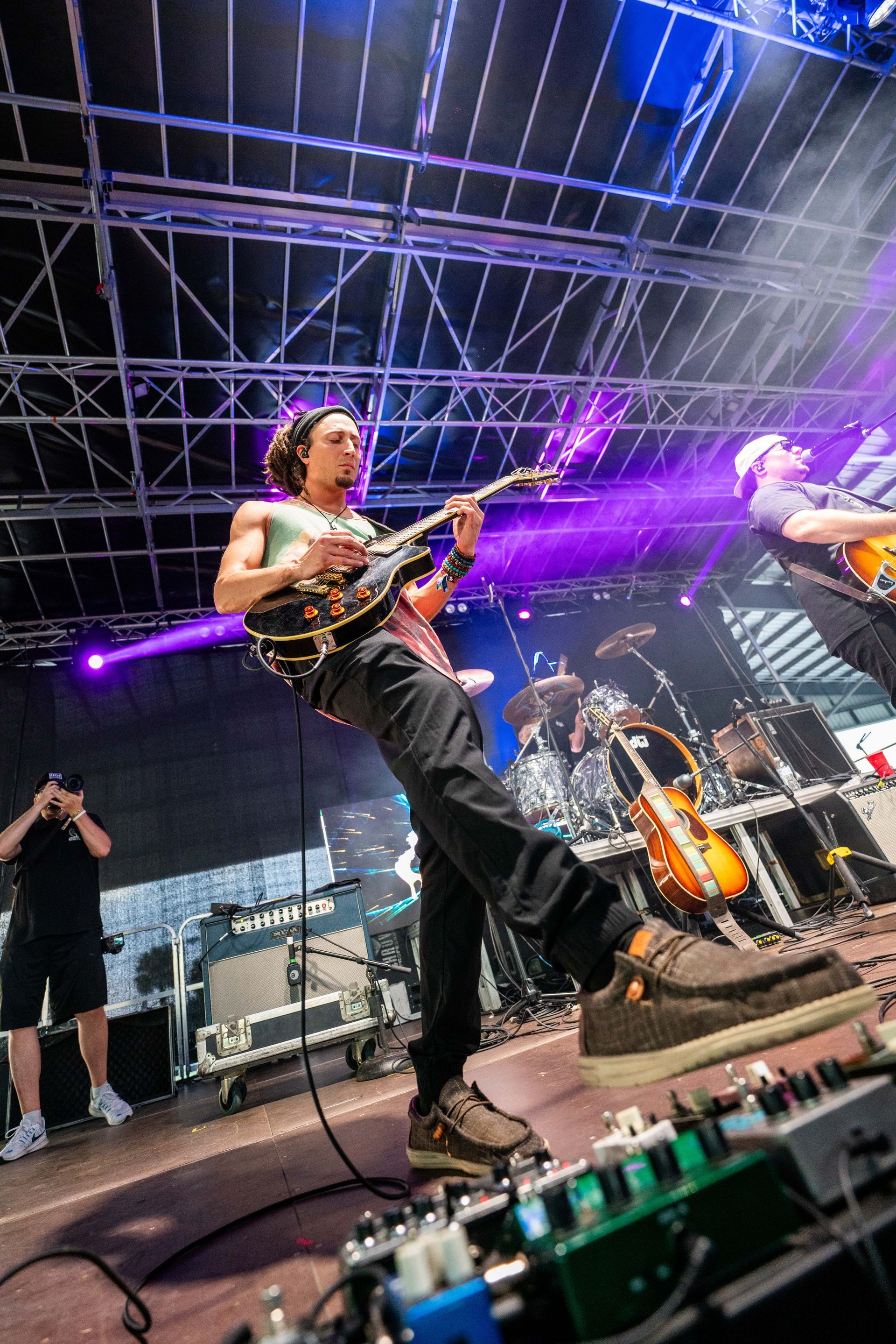 A man is playing a guitar on a stage with a band behind him.