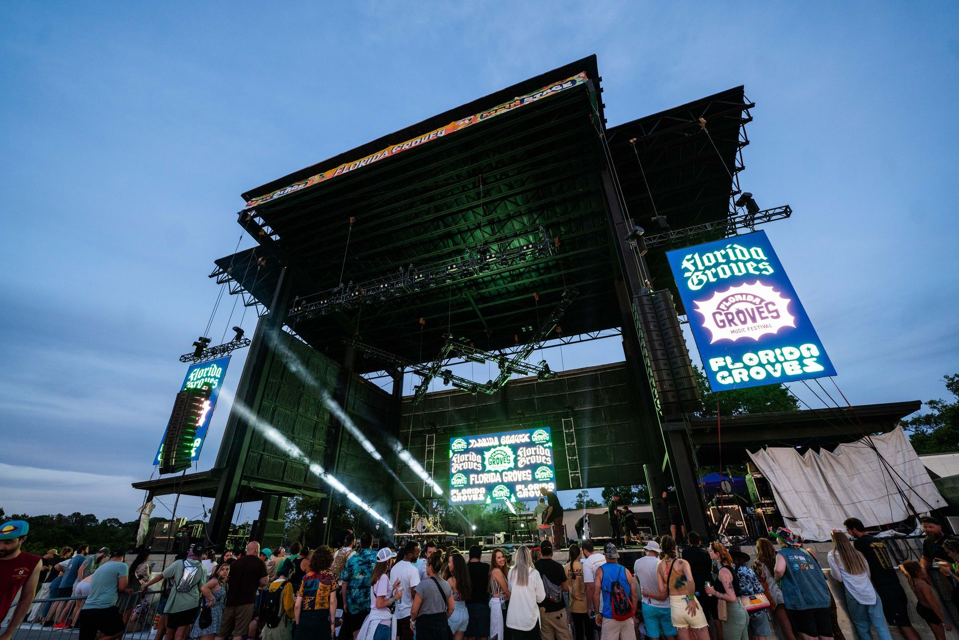 A crowd of people are standing in front of a large stage at a music festival.