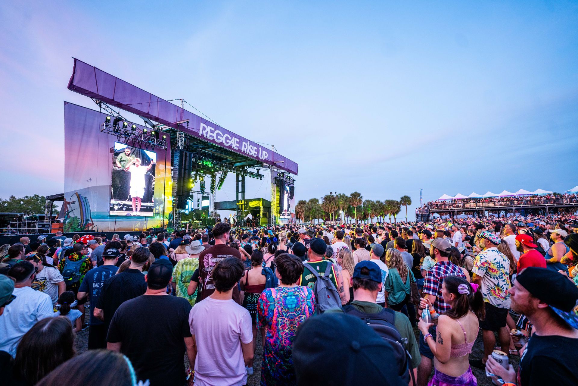 A crowd of people are standing in front of a stage at a music festival.