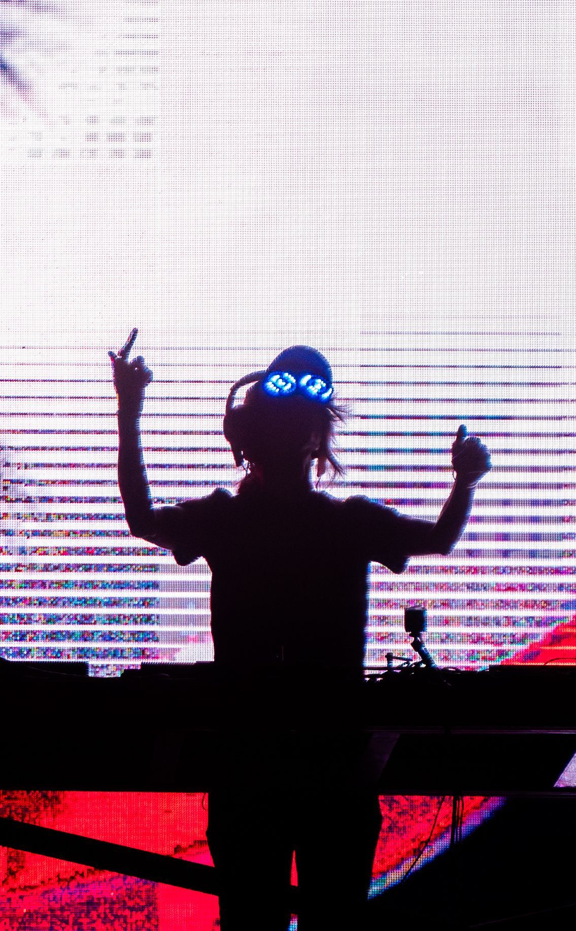 A silhouette of a dj standing in front of a large screen.