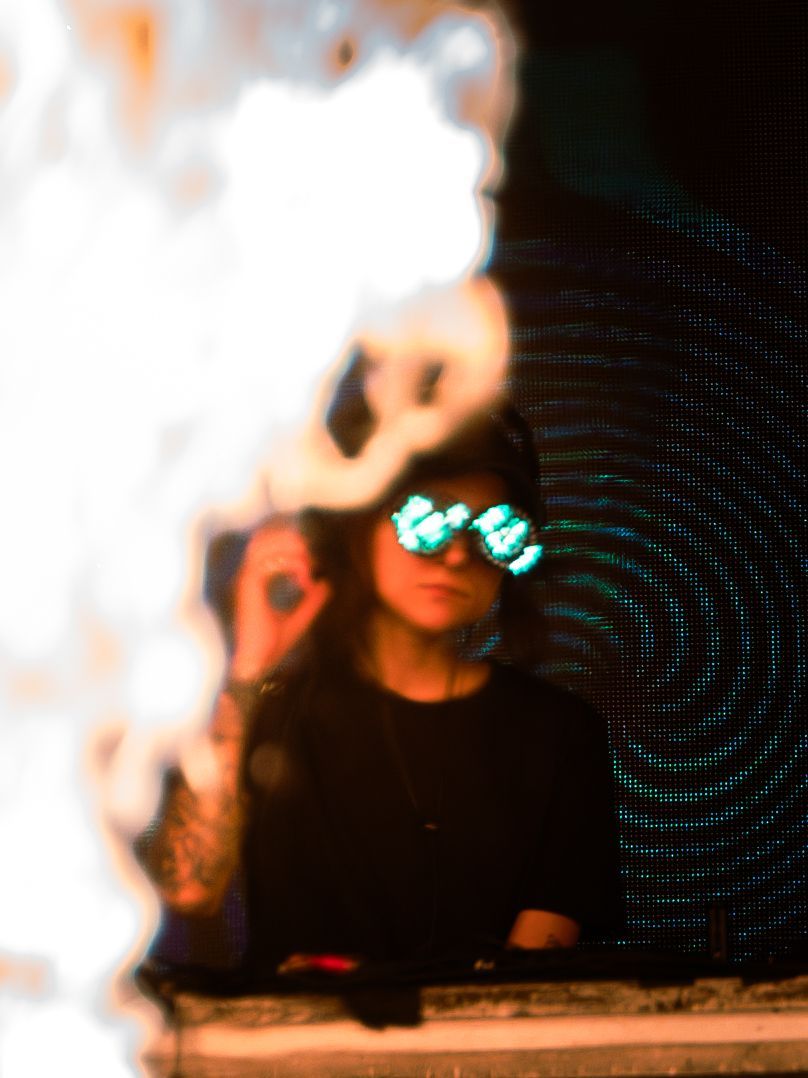 A woman wearing glow in the dark glasses is standing in front of a fire.
