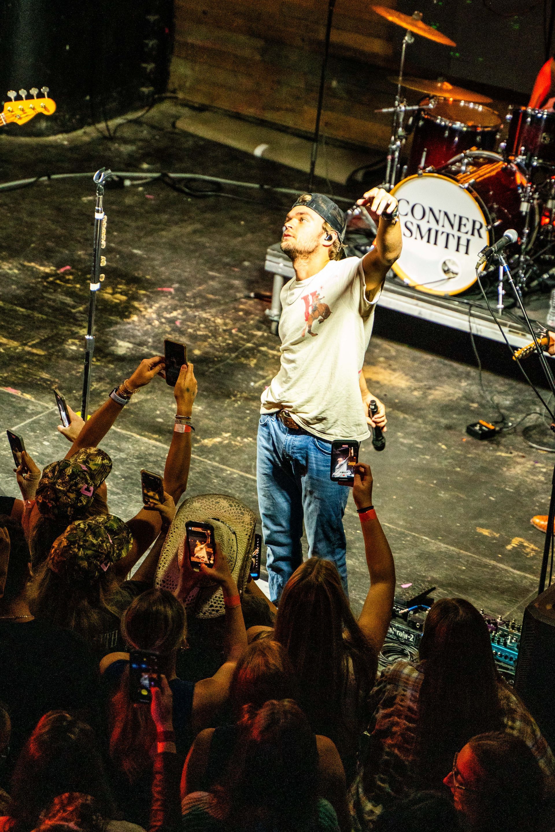 A man is singing into a microphone in front of a drum set that says ' turner smith ' on it