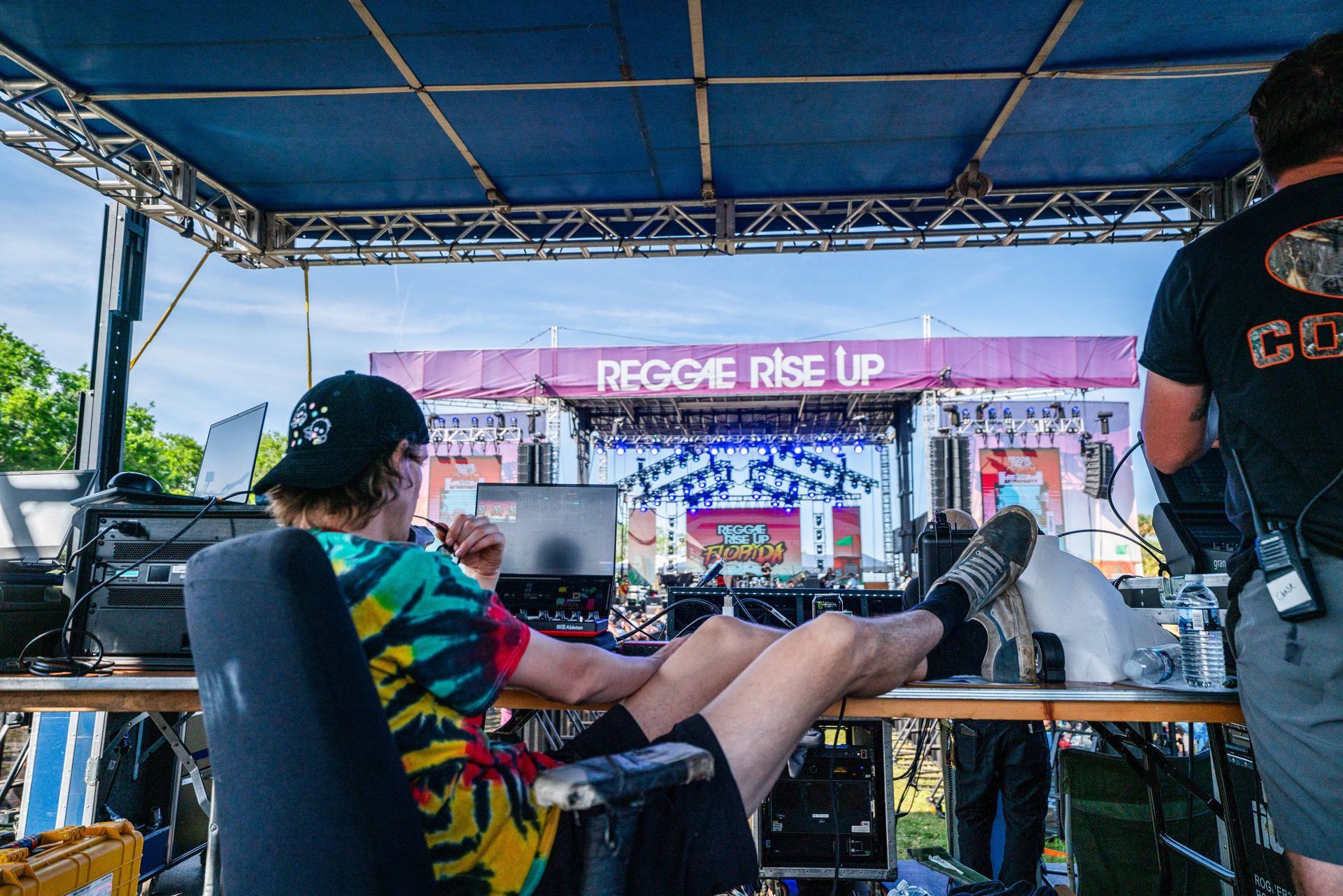 A man is sitting at a desk with his feet up in front of a stage that says reggae rise up.