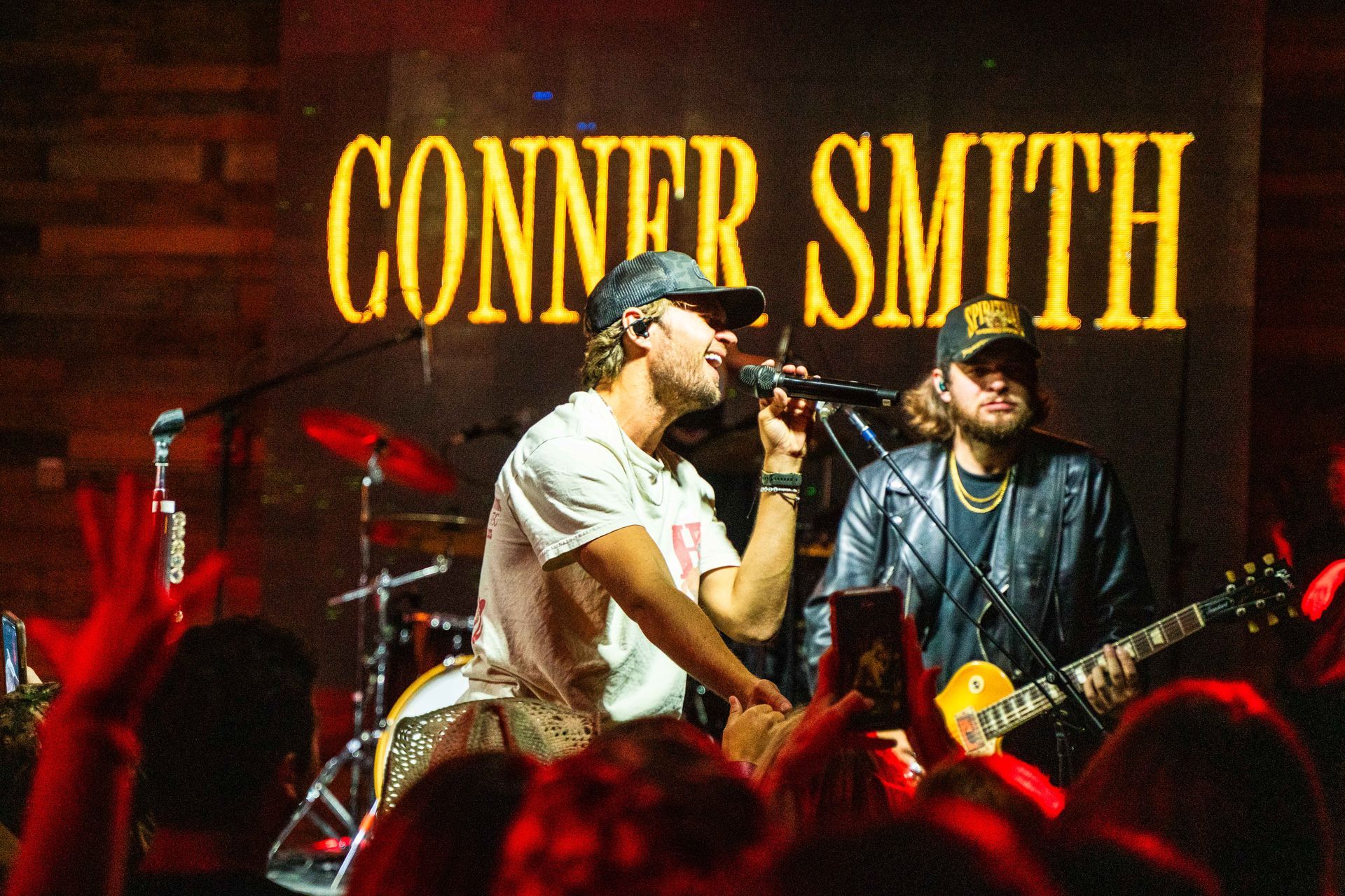 A man singing into a microphone in front of a sign that says conner smith