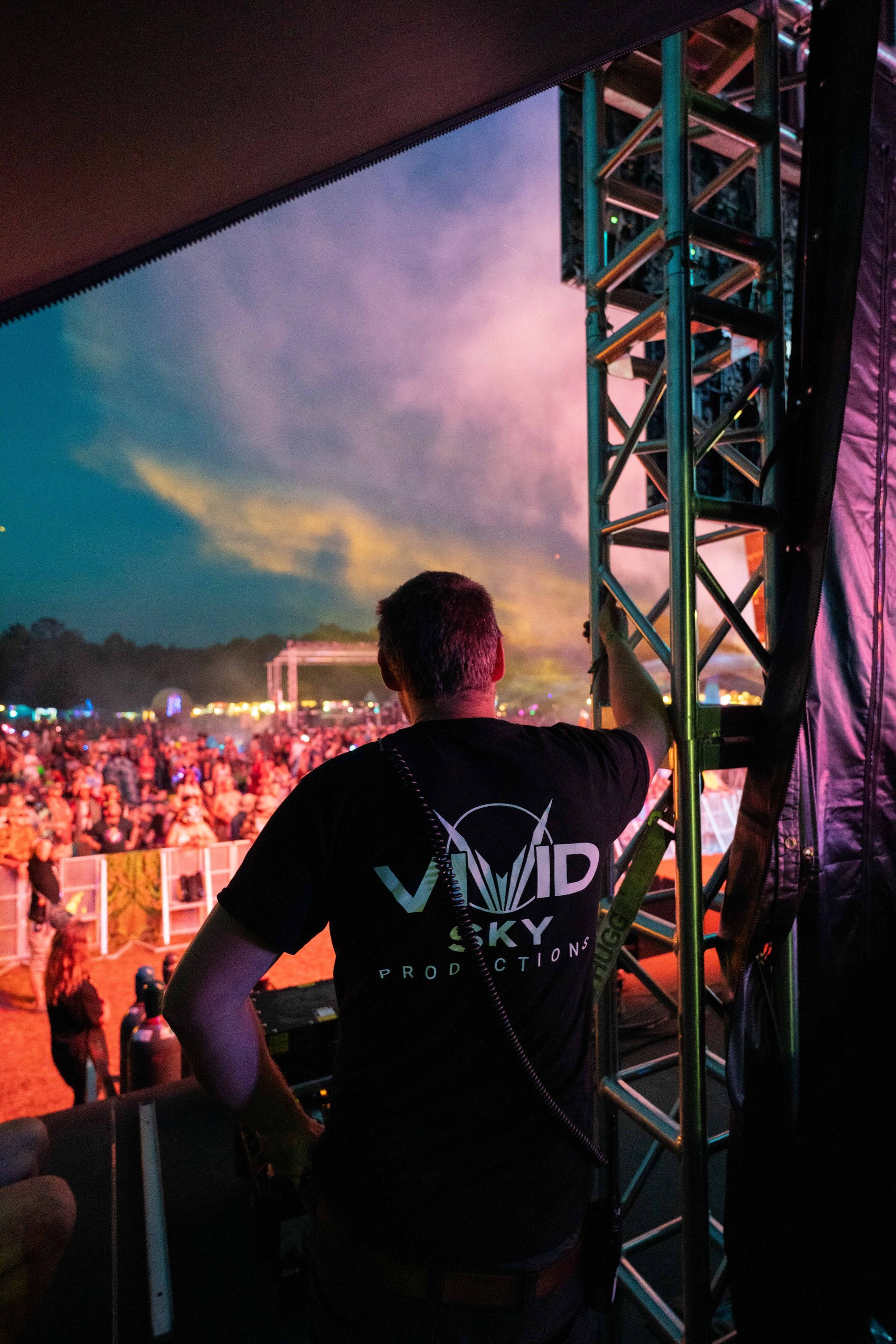 A man in a vivid sky t-shirt is standing in front of a crowd at a concert.