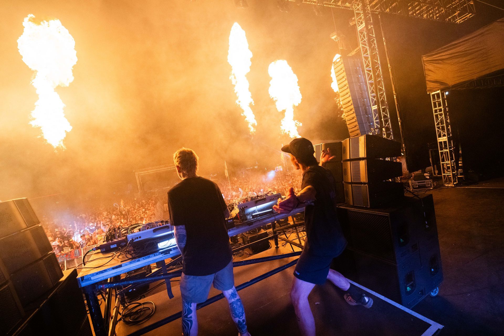 Two men are standing on a stage playing instruments in front of a crowd.