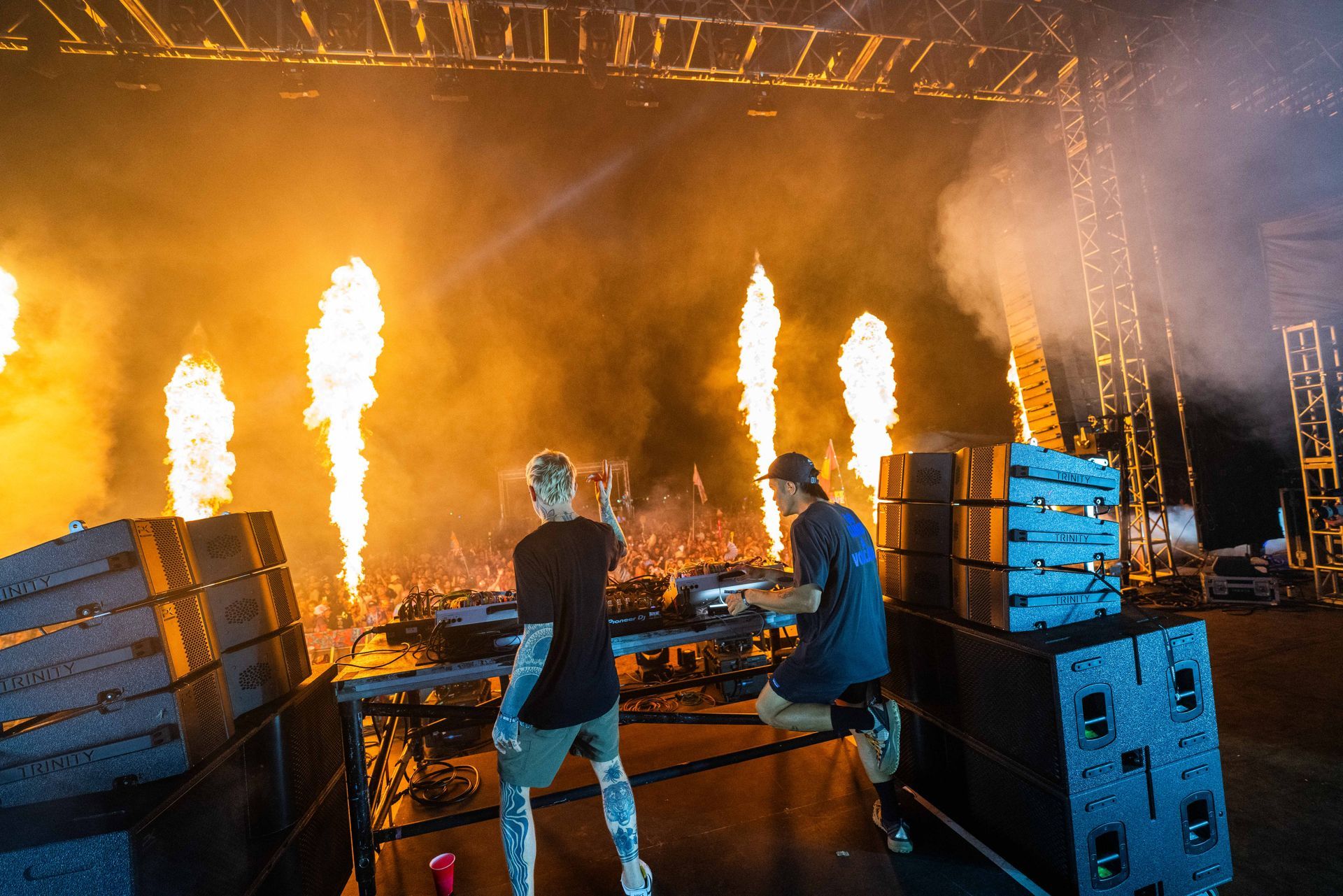 Two men are playing instruments on a stage with flames coming out of the stands.
