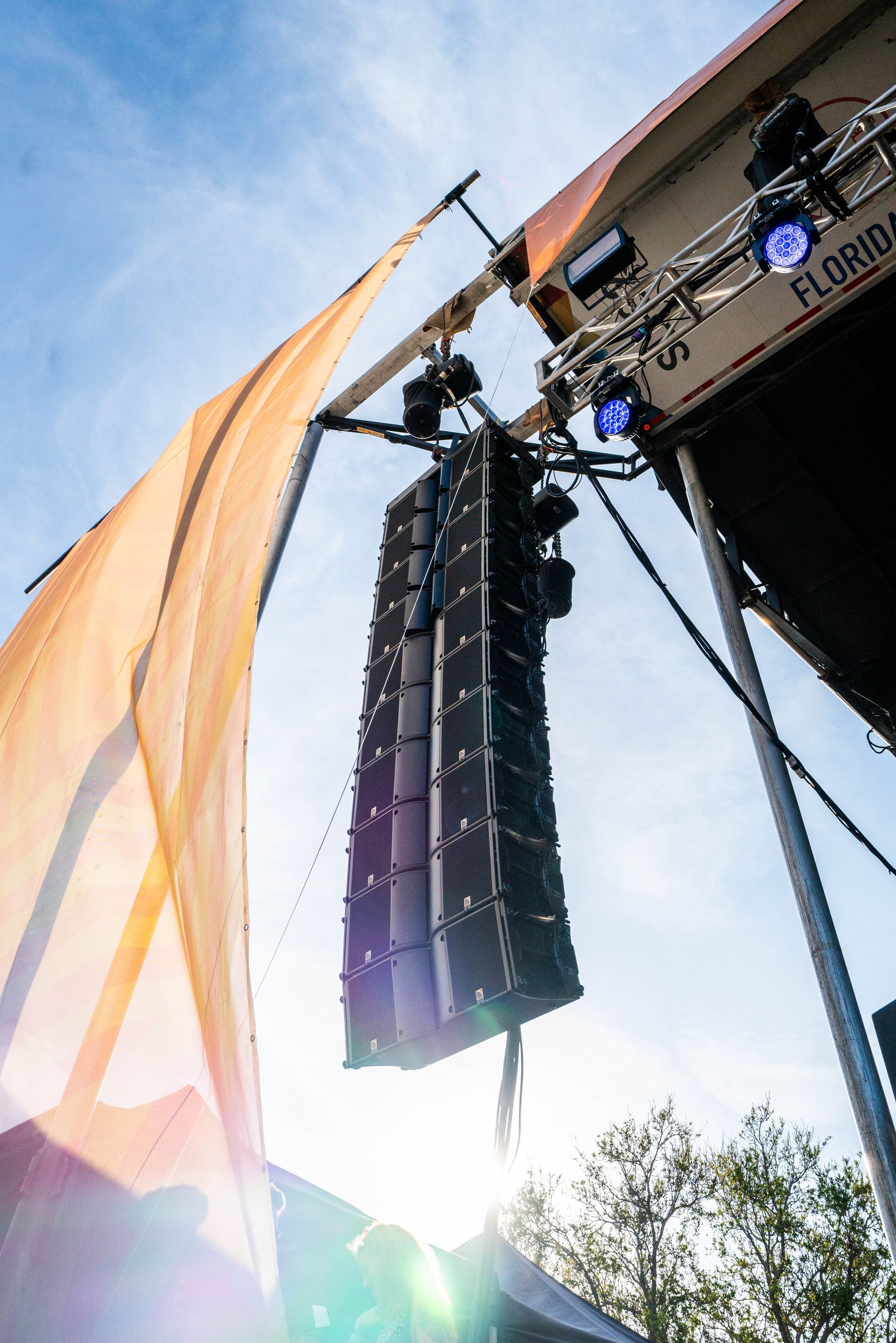 A large speaker is hanging from the ceiling of a stage.