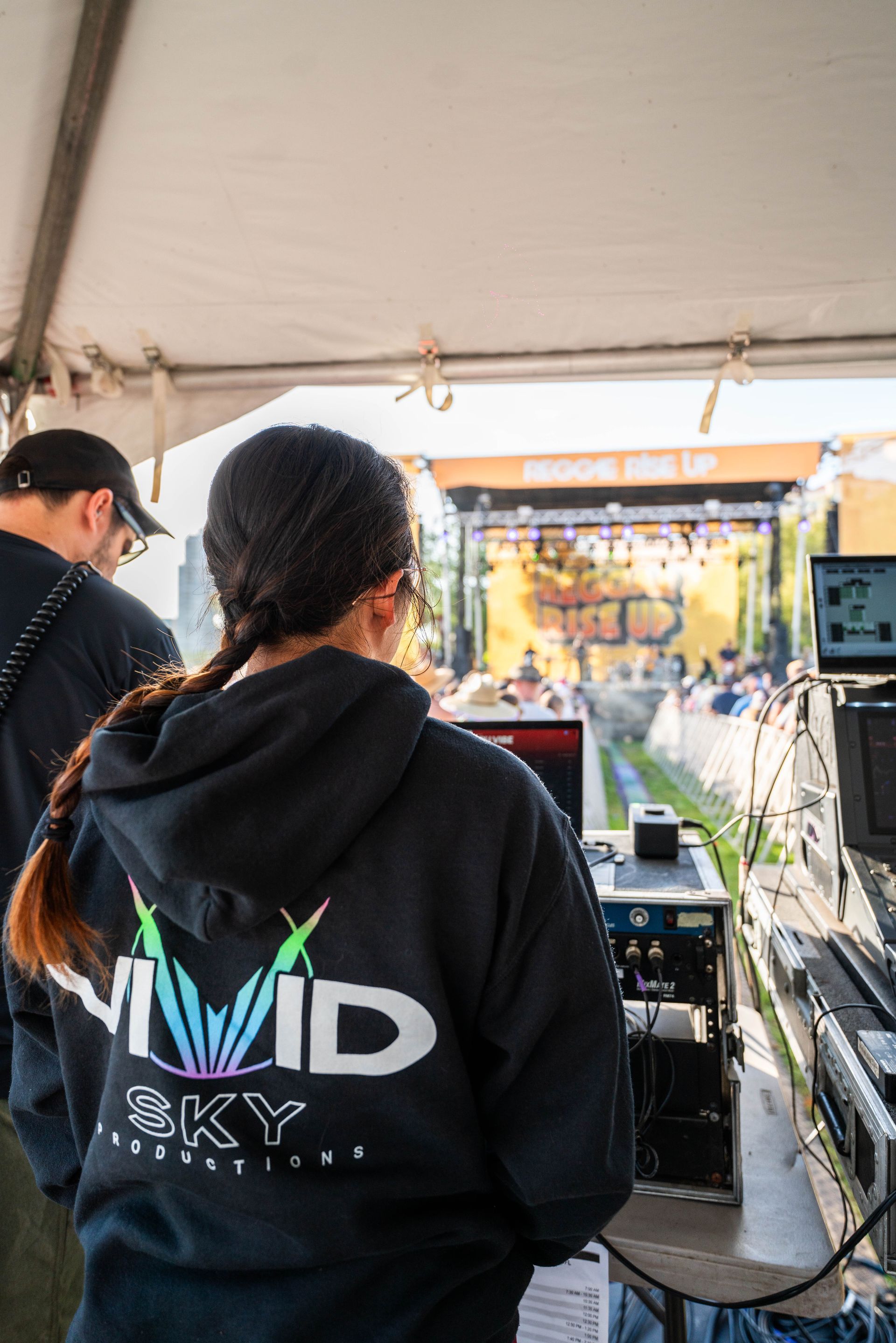 A woman wearing a black hoodie with the word vivid sky on the back is standing in front of a stage.