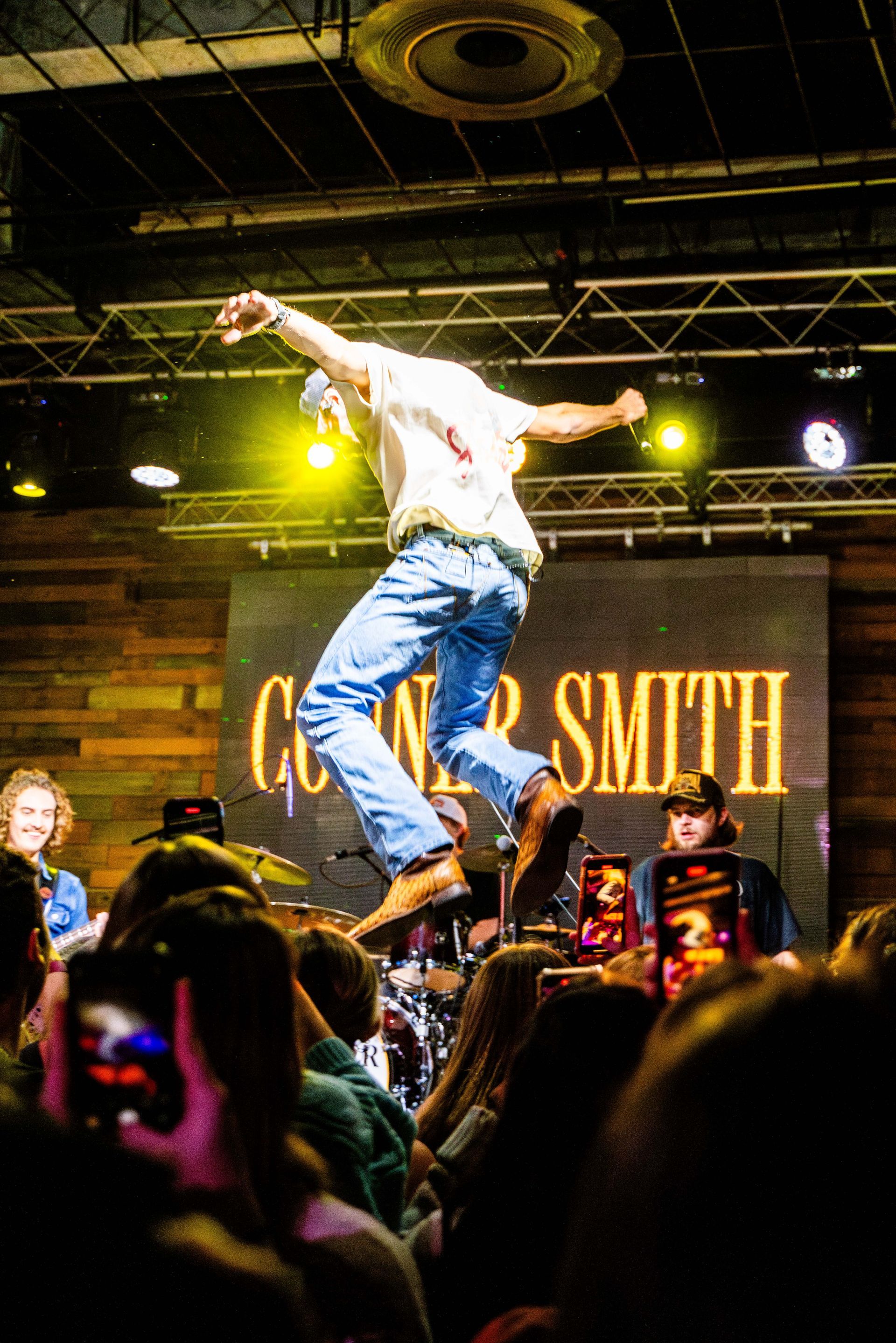 A man is jumping in the air on a stage in front of a crowd.