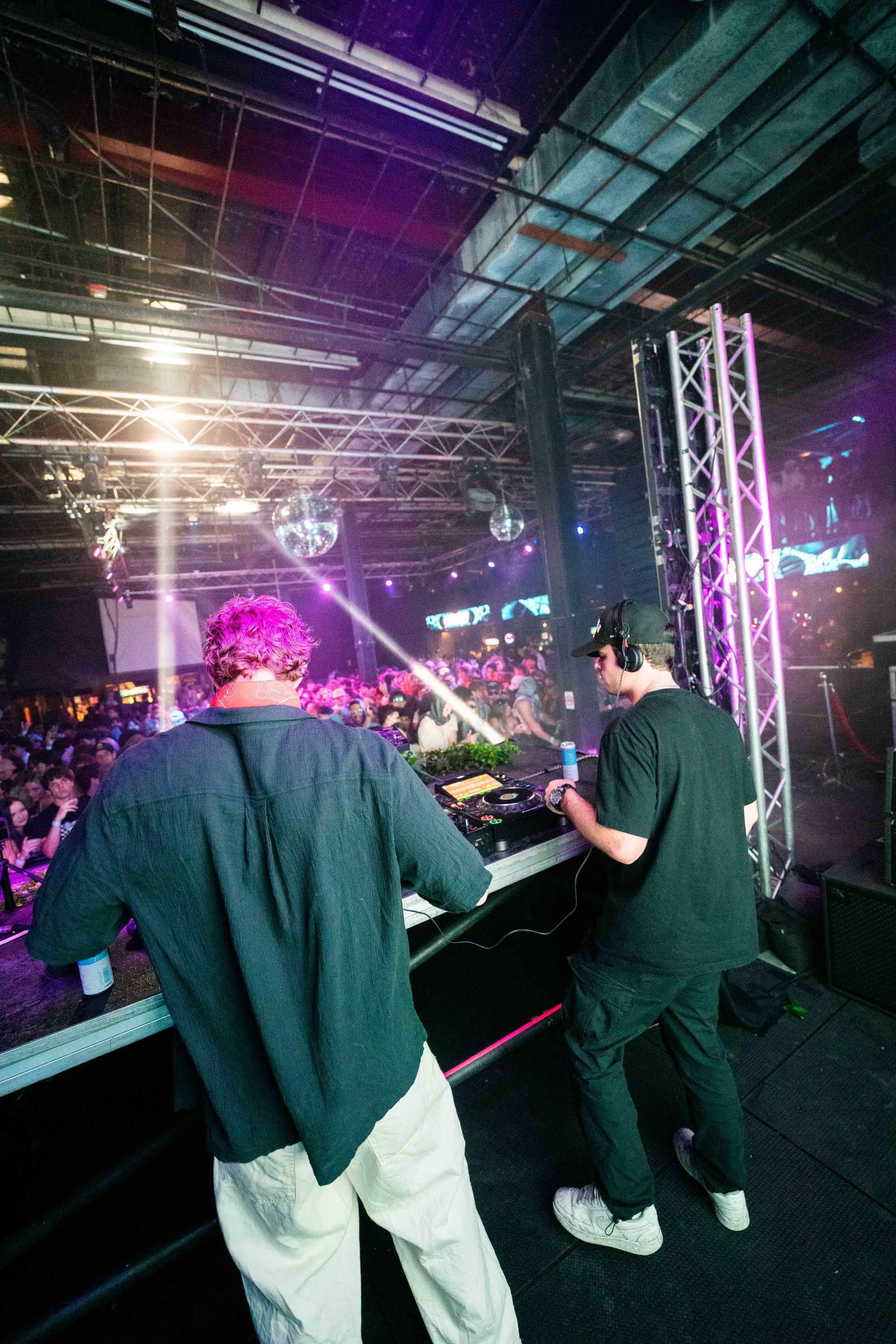 Two men are playing music on a stage in a club.