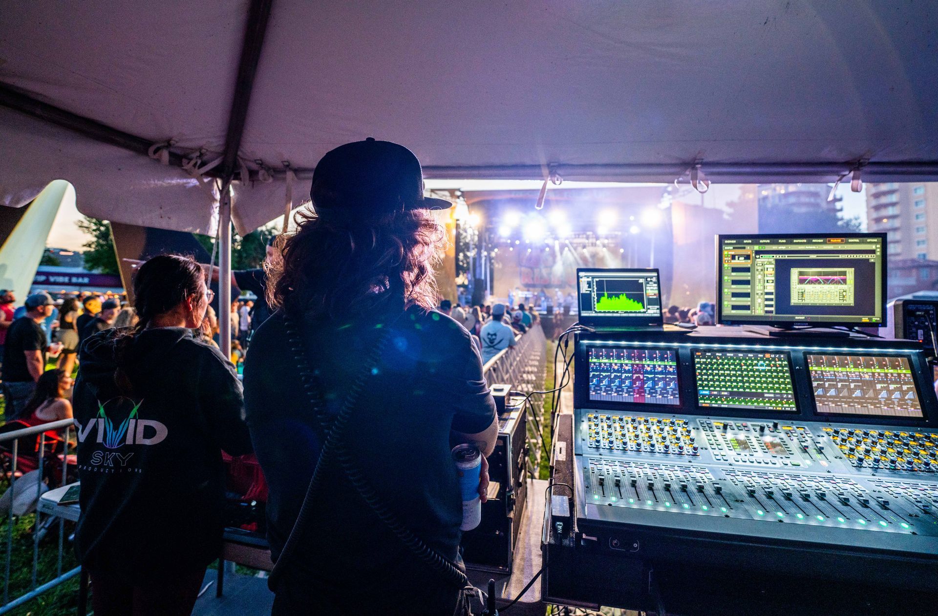 A man is standing in front of a mixer at a concert.