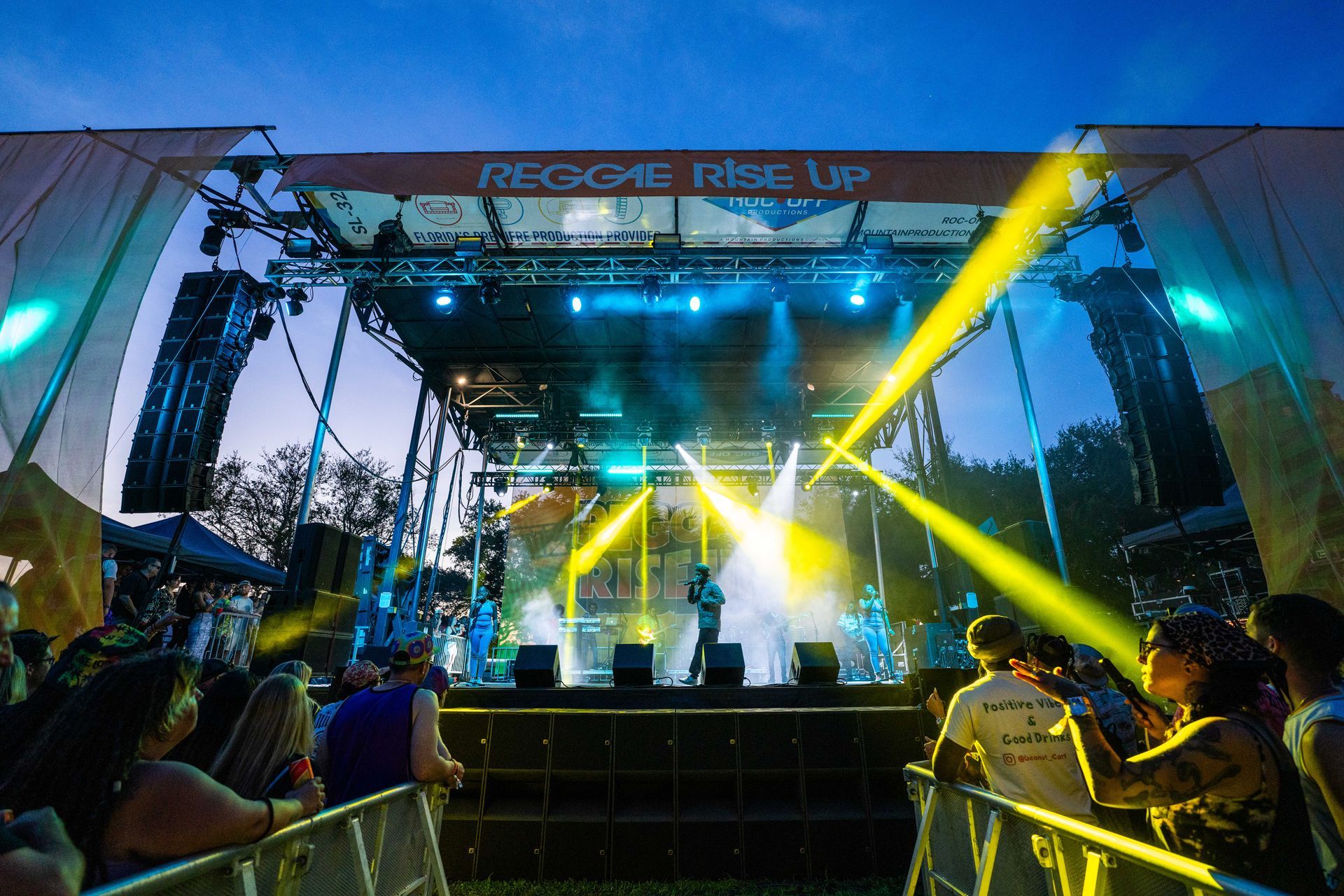 A group of people are standing in front of a stage that says reggae rise up