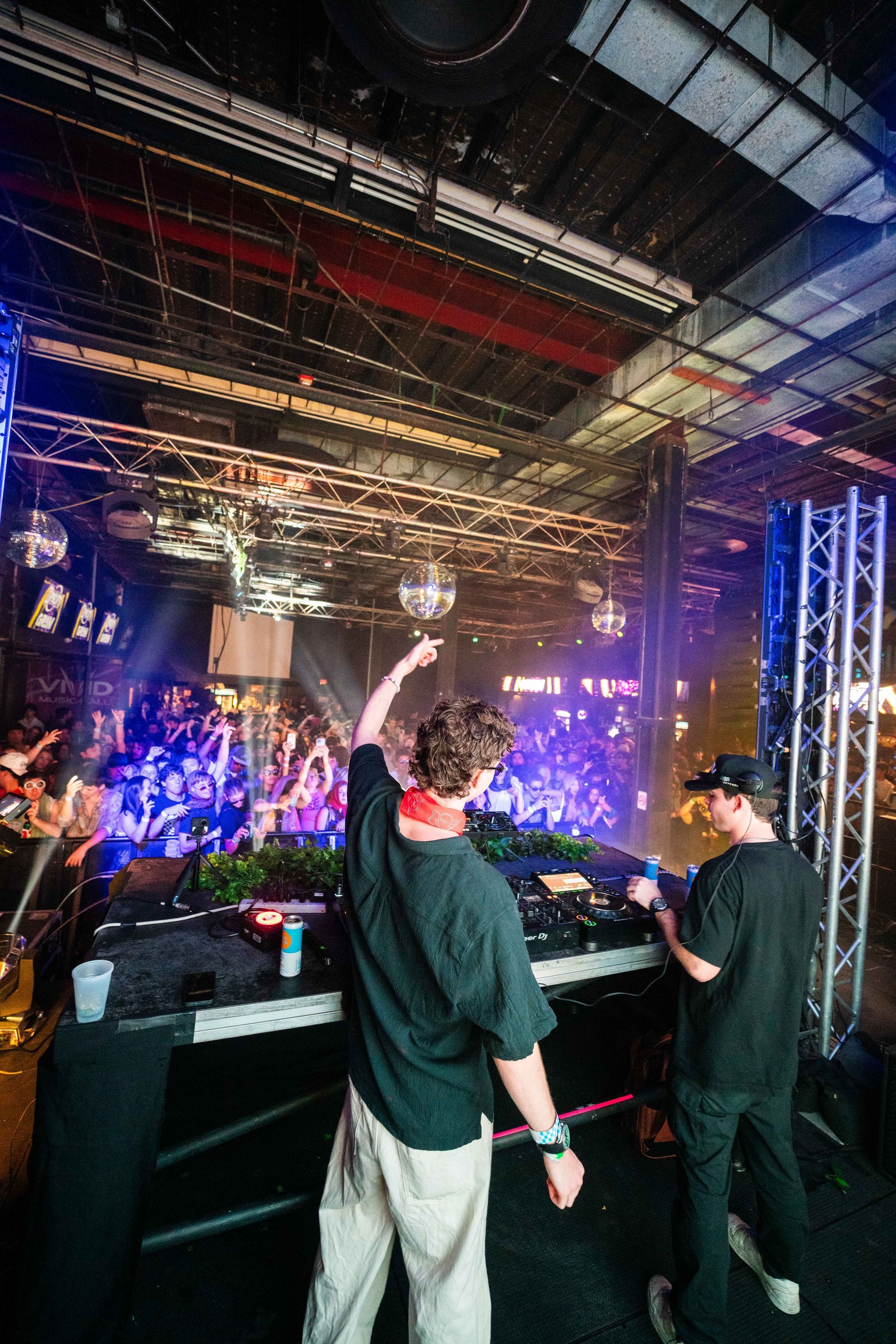 Two men are standing in front of a dj booth at a concert.