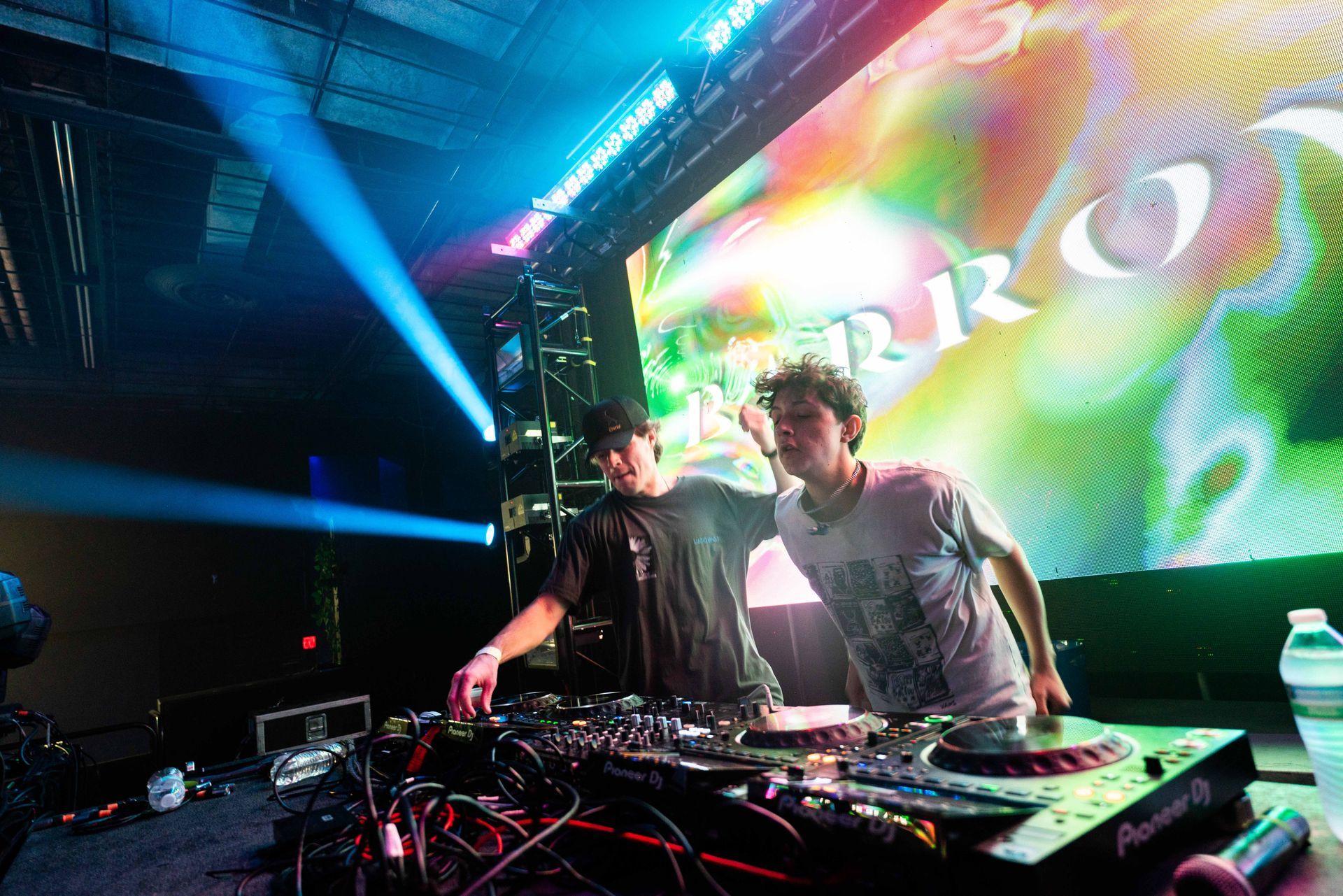 Two men are playing music on a stage in front of a large screen.