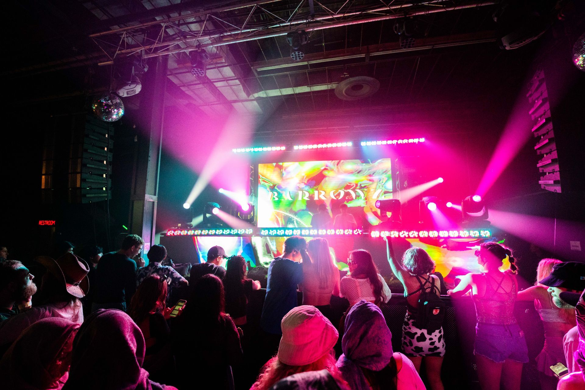 A crowd of people are dancing in front of a large screen that says friday