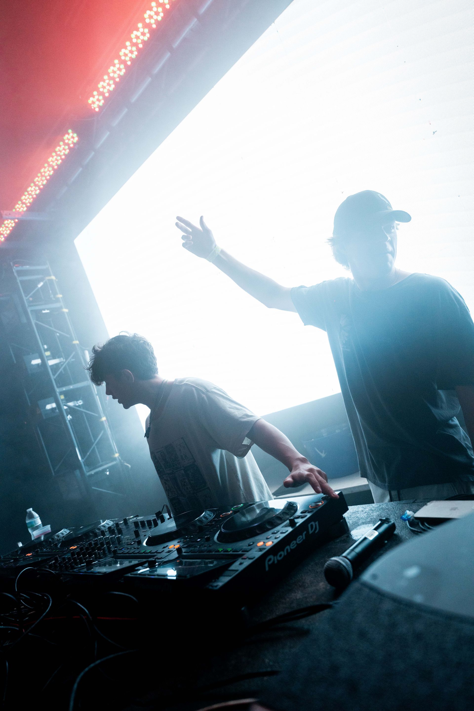 Two men are playing music on a stage in front of a large screen.