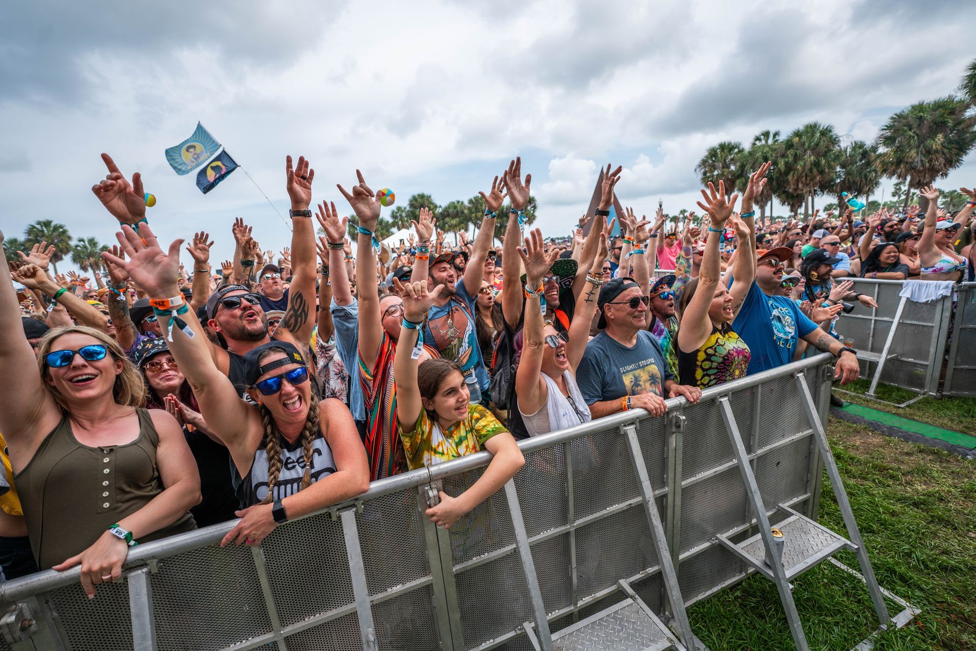 A crowd of people standing behind a fence at a concert with their hands in the air.