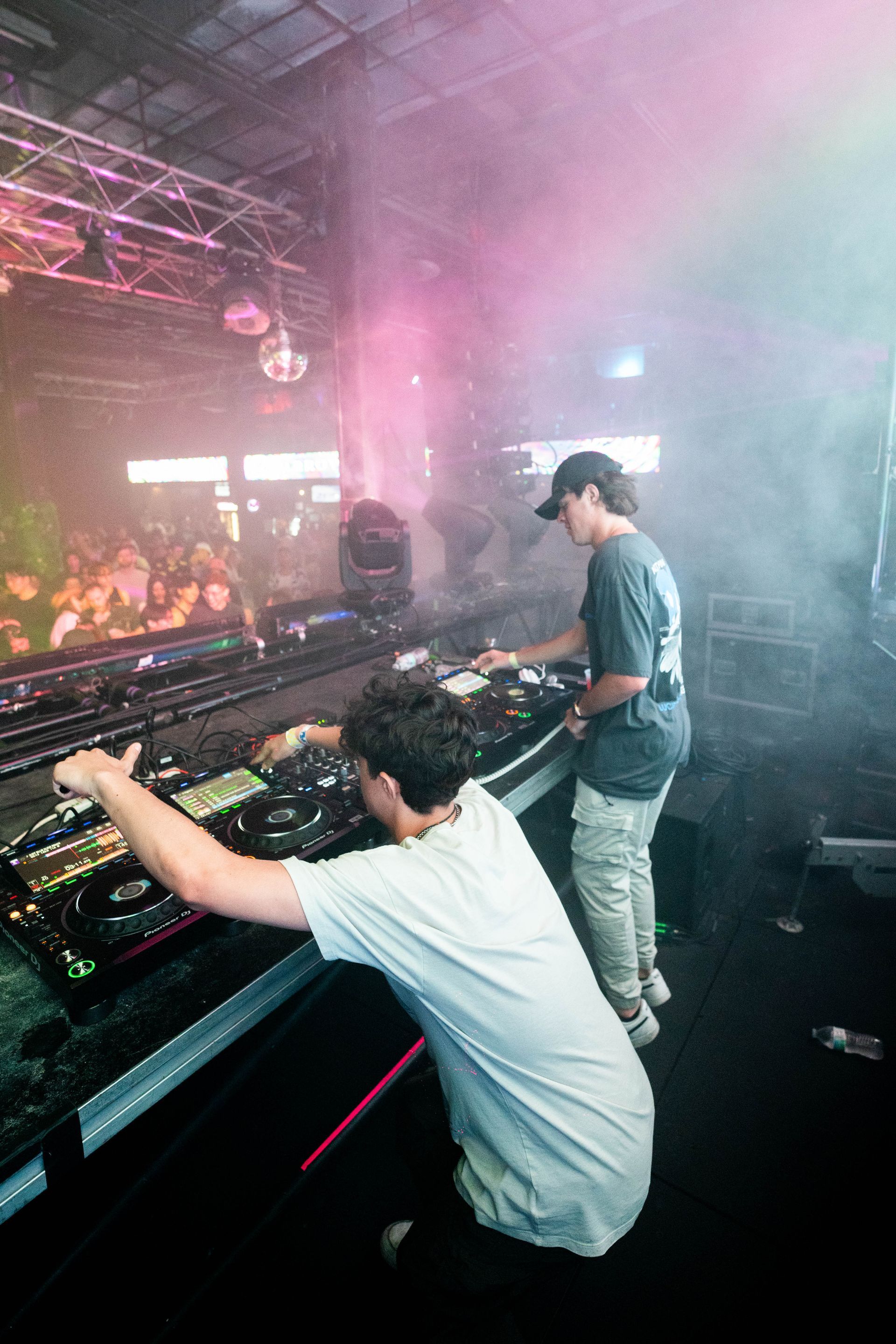 Two men are playing music on a stage in a club.