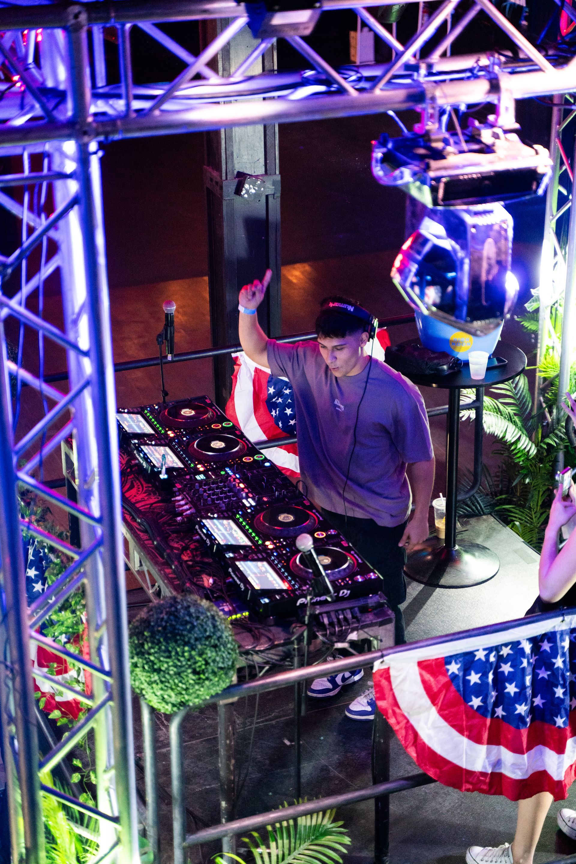 A man is standing in front of a dj booth with an american flag in the background.
