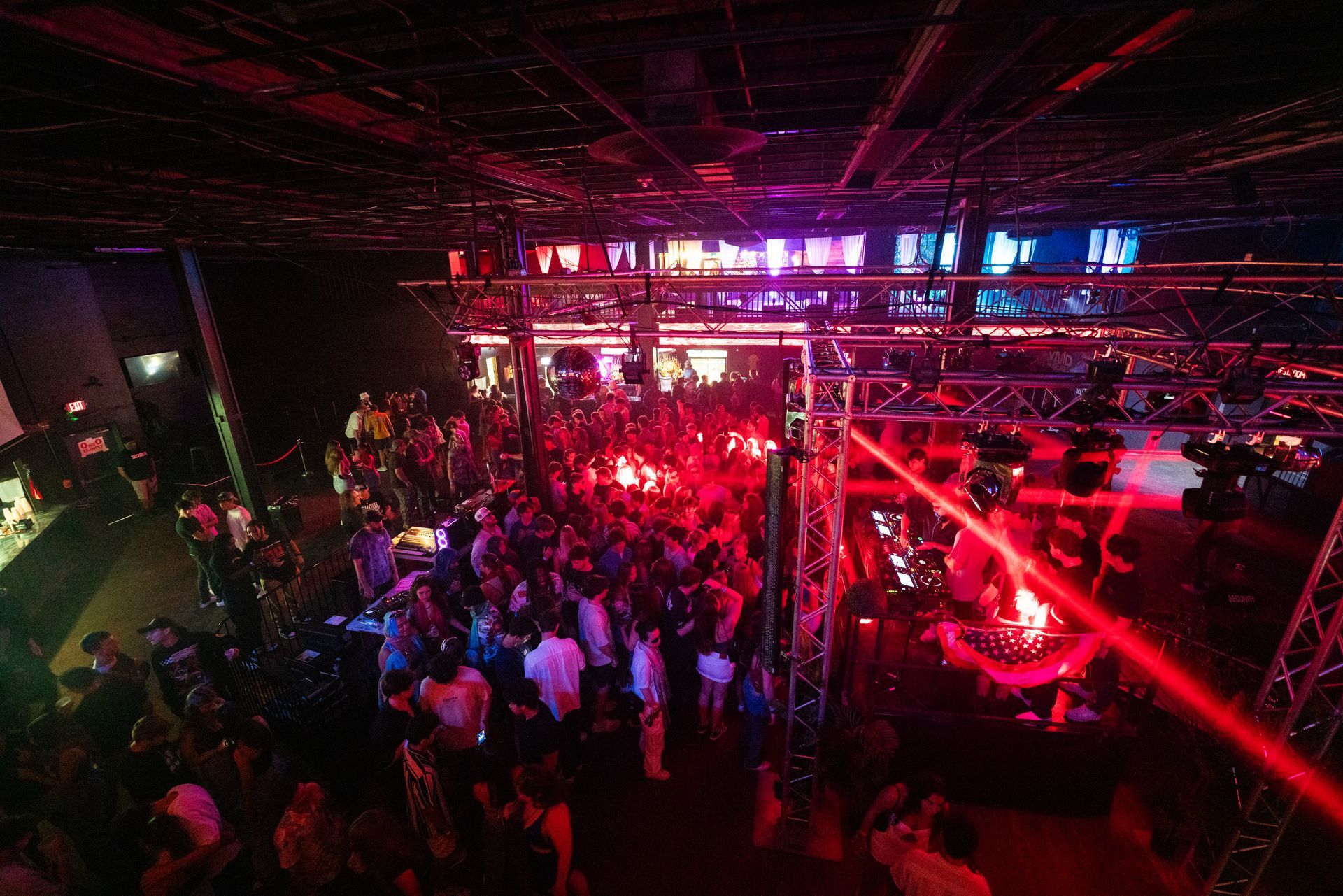 A crowd of people are dancing in a club with red lights.