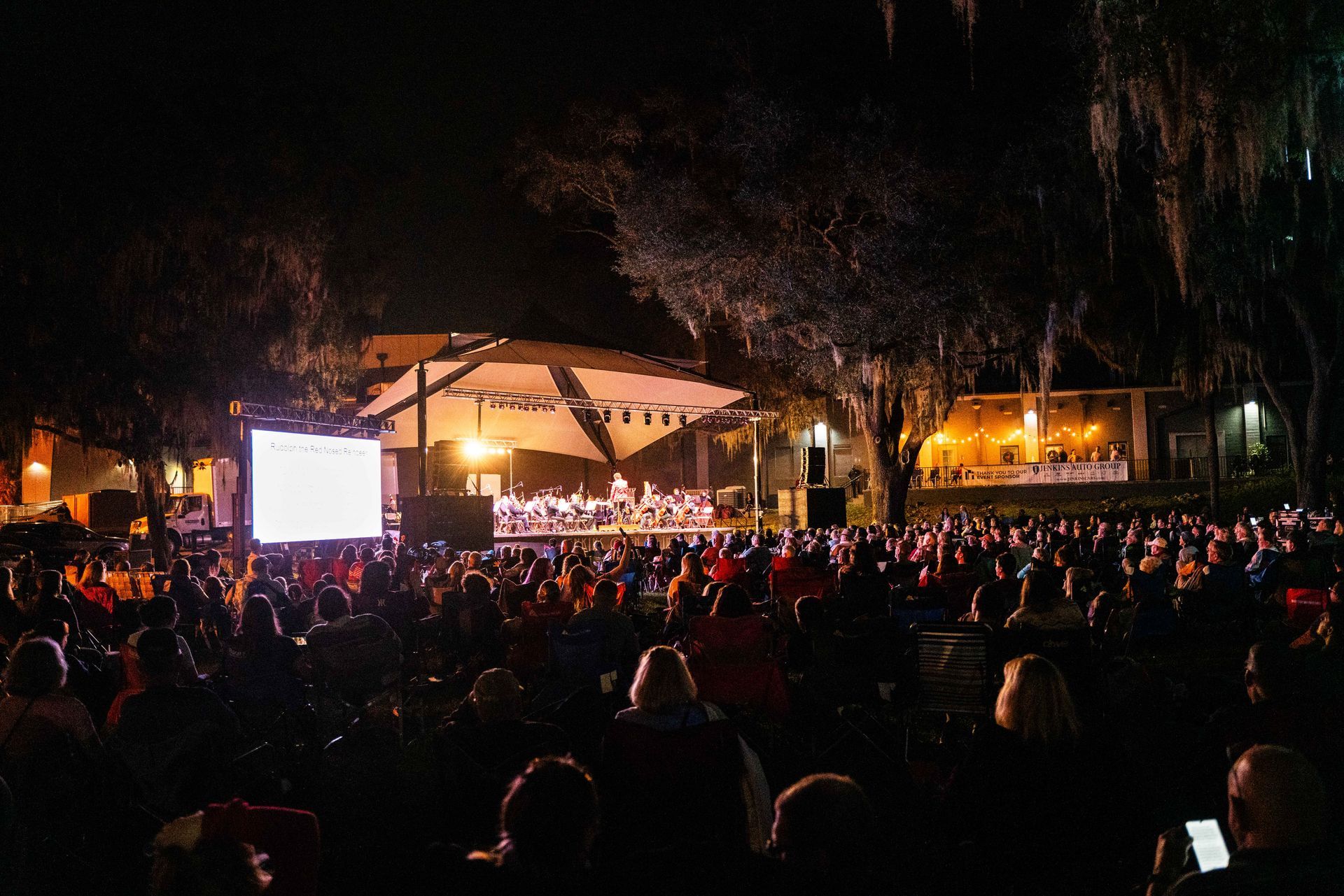 A large crowd of people are sitting in front of a stage at night.