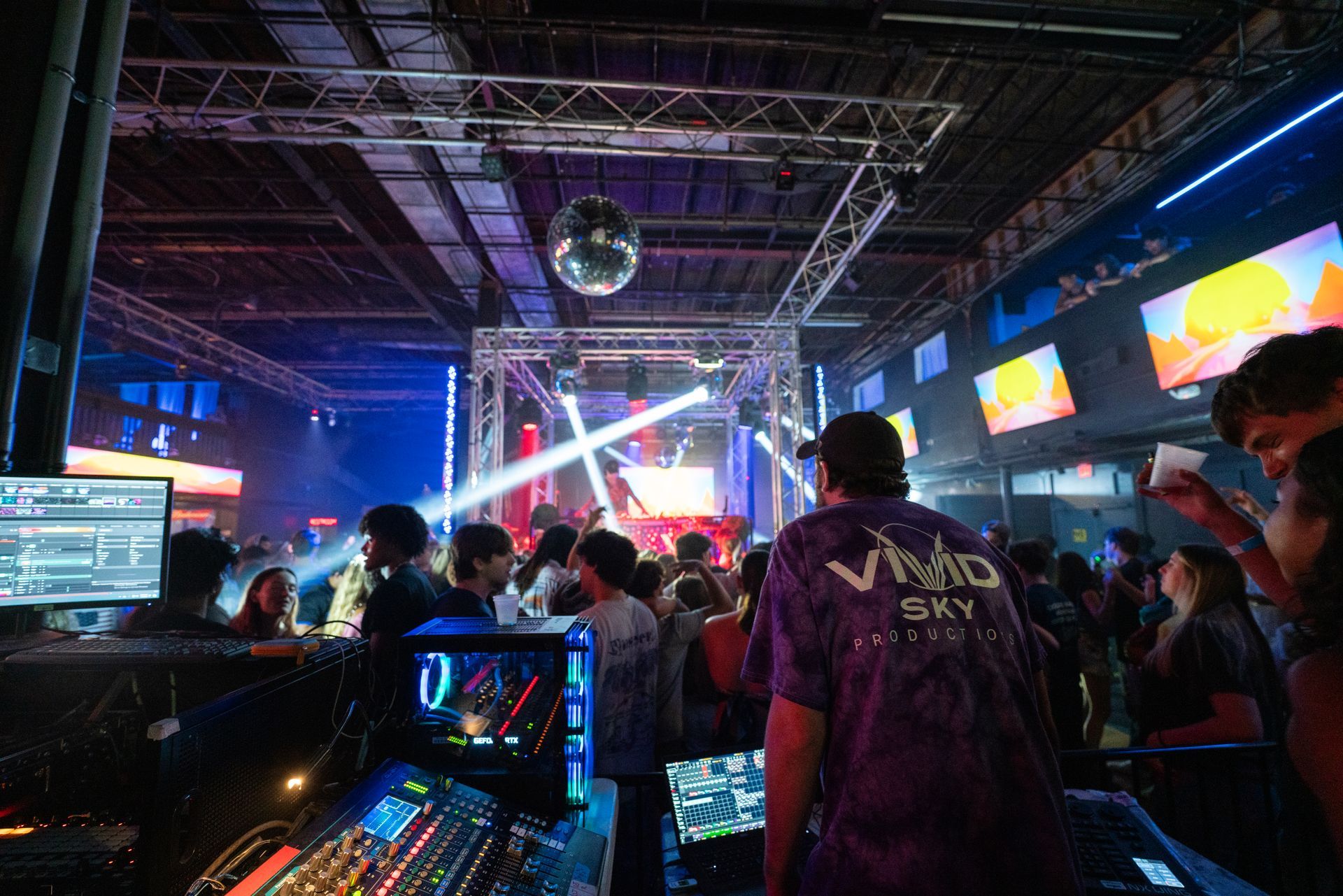 A man in a purple shirt is standing in front of a crowd of people in a club.