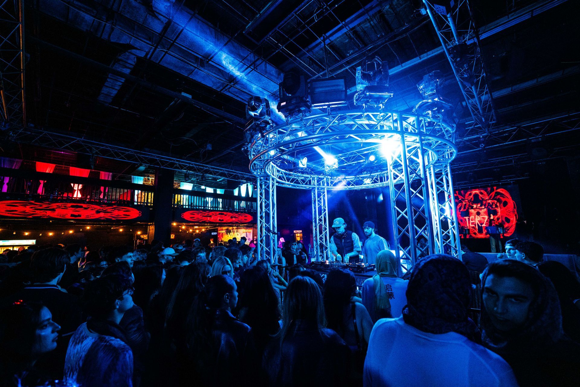 A crowd of people are gathered in a dark room with blue lights