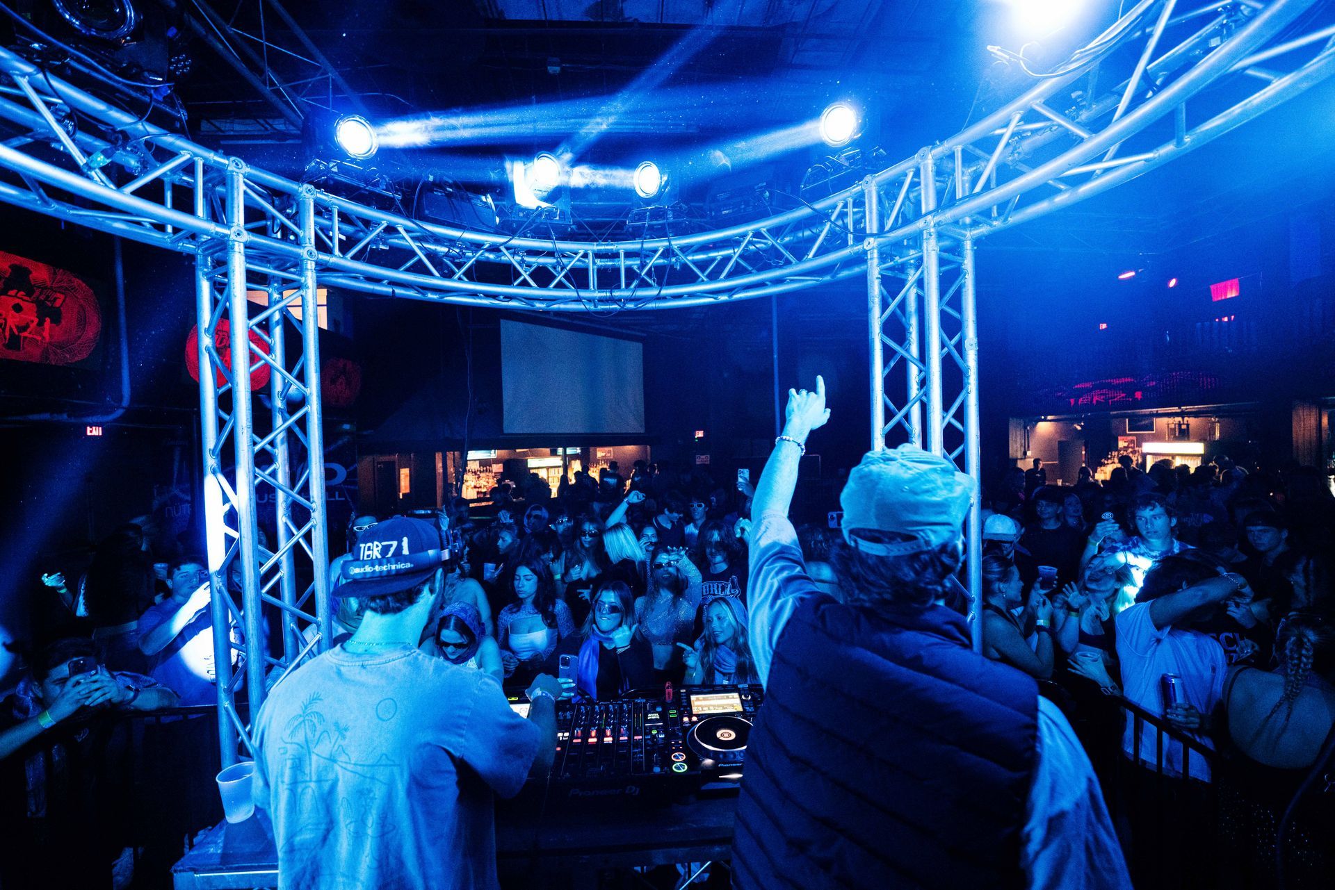 Two men are playing music in front of a crowd in a club.